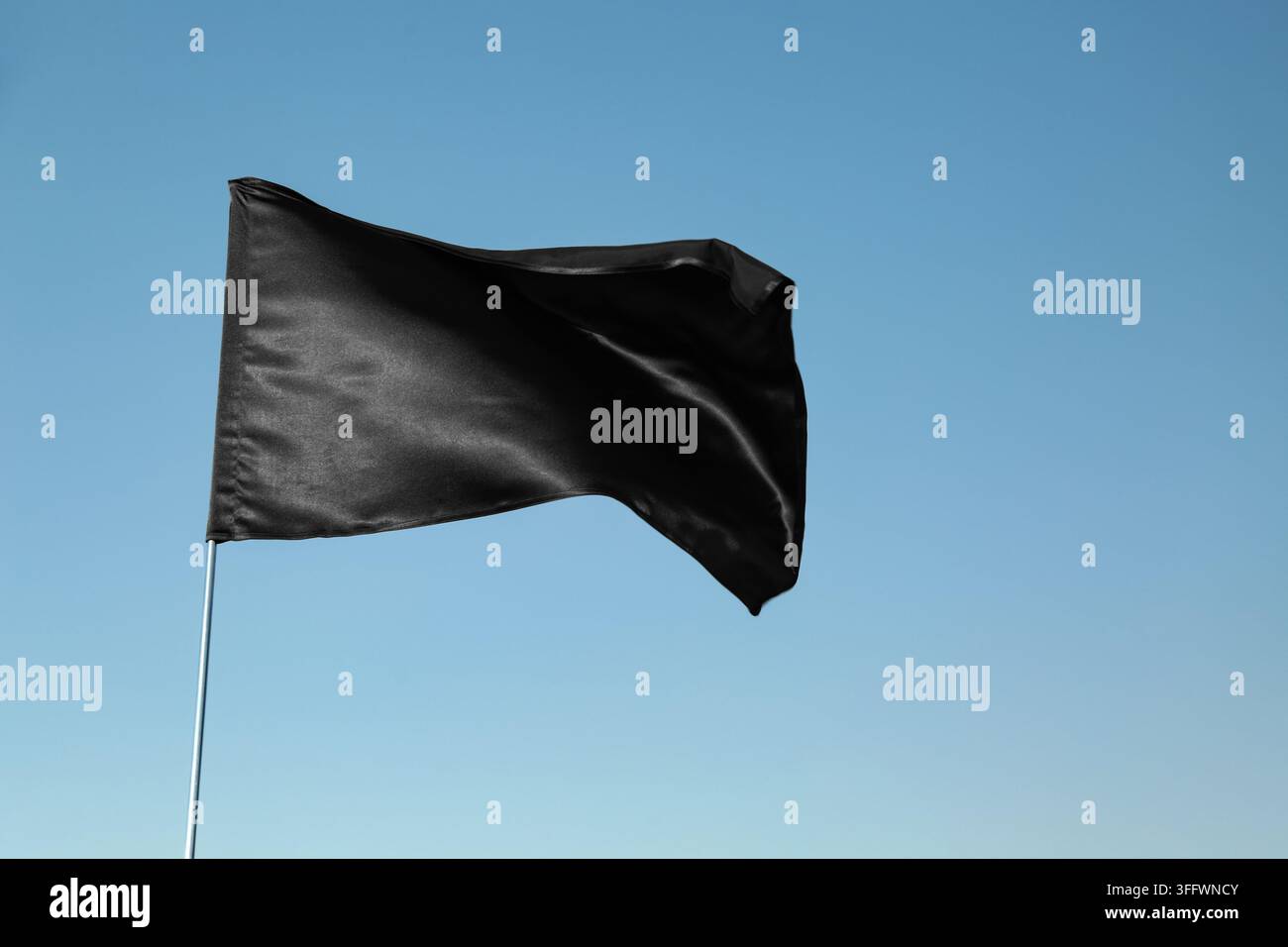 Drapeau noir de protestation et de deuil flottant dans le vent sous un ciel bleu clair en signe de chagrin, d'anarchie ou de résistance politique et de mouvement social Banque D'Images