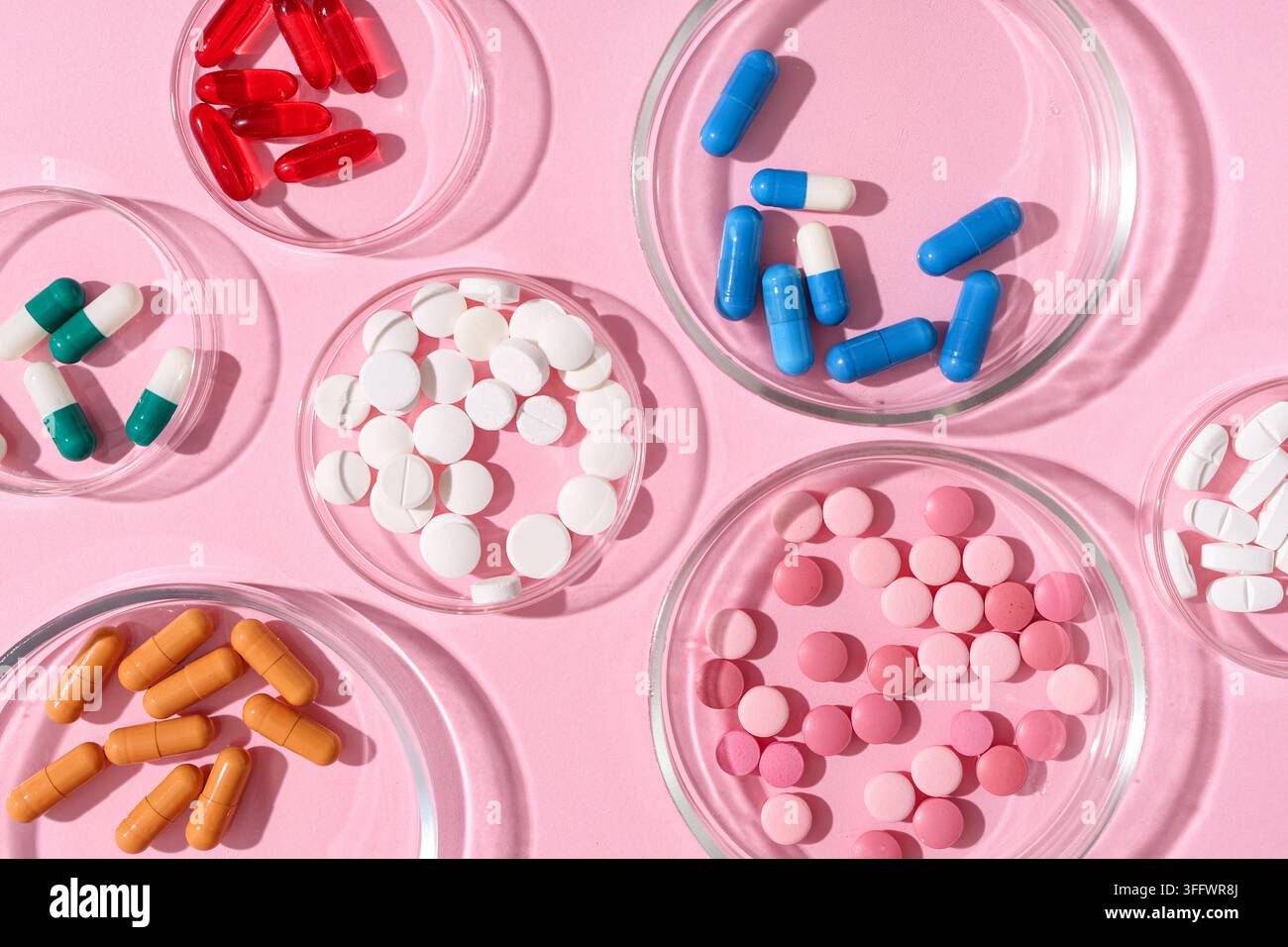 Crise sanitaire et industrie pharmaceutique, diverses pilules et capsules colorées dans des boîtes de Pétri sur un fond rose pour la recherche médicale et le traitement Banque D'Images