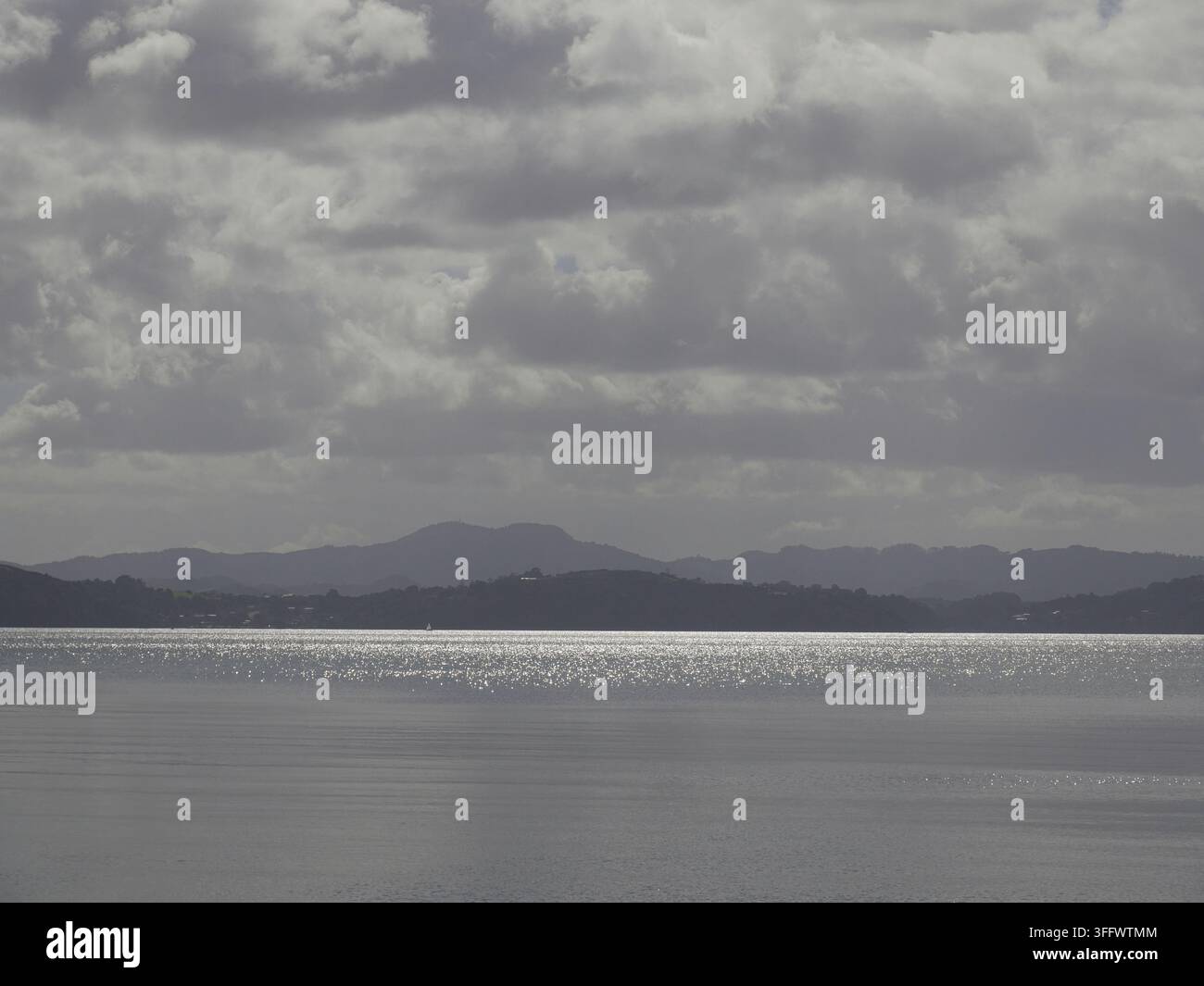 Vue calme de la côte avec une surface de l'eau miroitante sous un ciel nuageux dramatique et des caps lointains ondulant à l'horizon. Banque D'Images