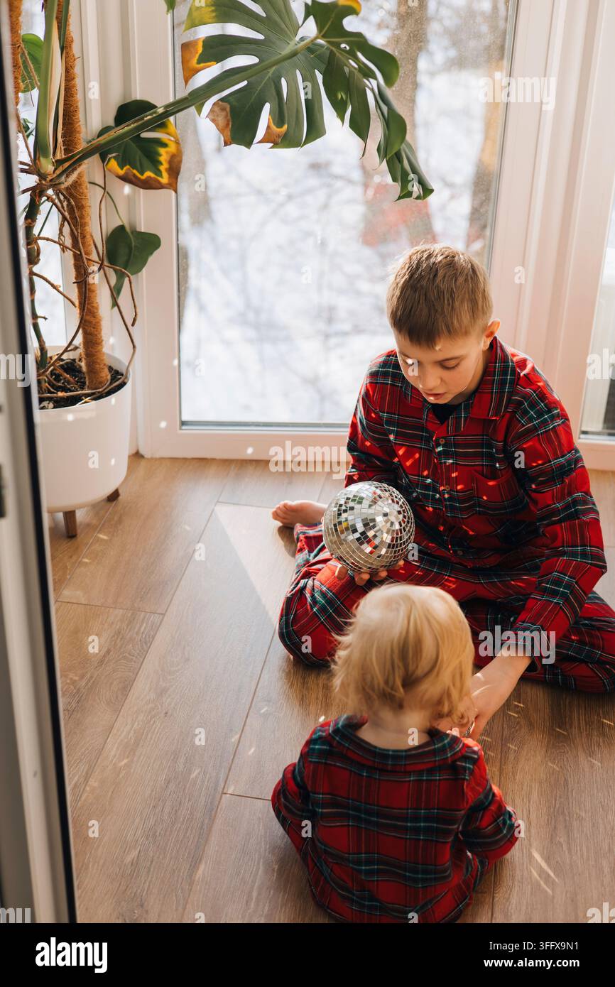 Deux frères en pyjamas à carreaux assortis jouant avec des décorations de Noël à la maison Banque D'Images