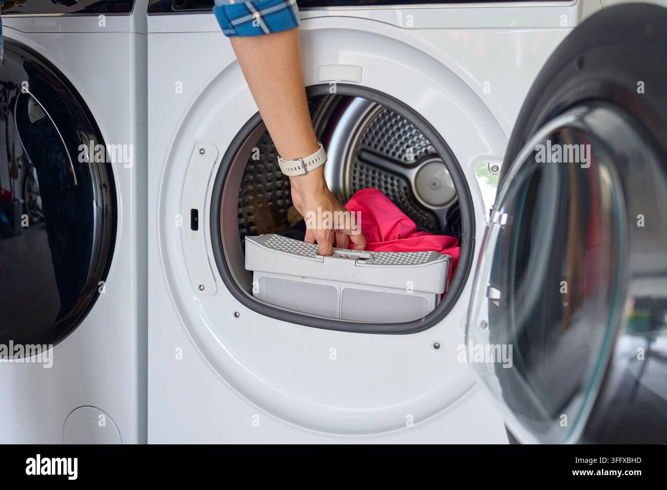 Main tirant le filtre à peluches d'un sèche-linge ouvert avec des vêtements dans le tambour. Nettoyage régulier du sèche-linge Banque D'Images