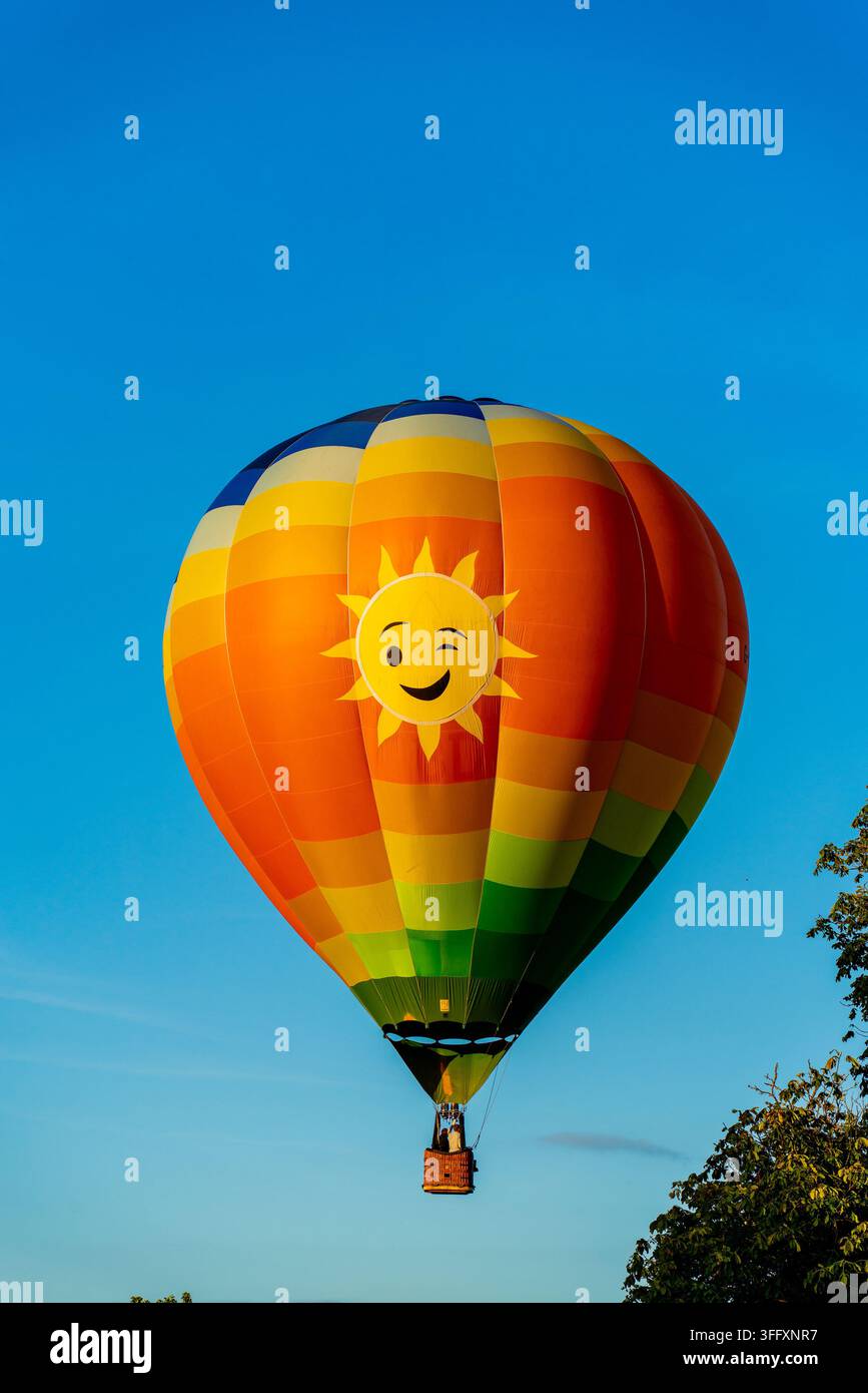 Bakewell, Royaume-Uni - 05 septembre 2026 : Vue d'un ballon à air chaud coloré arborant un visage de soleil clignotant, flottant contre un ciel bleu clair. Banque D'Images