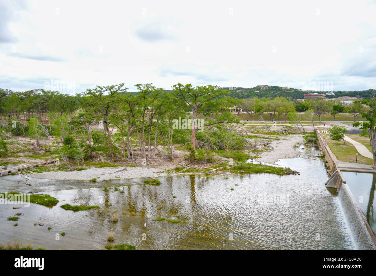 La rivière Guadalupe coulant sur un bas barrage en béton à côté de berges rocheuses, de chemins riverains et d'arbres à Kerrville, Texas, États-Unis. Banque D'Images