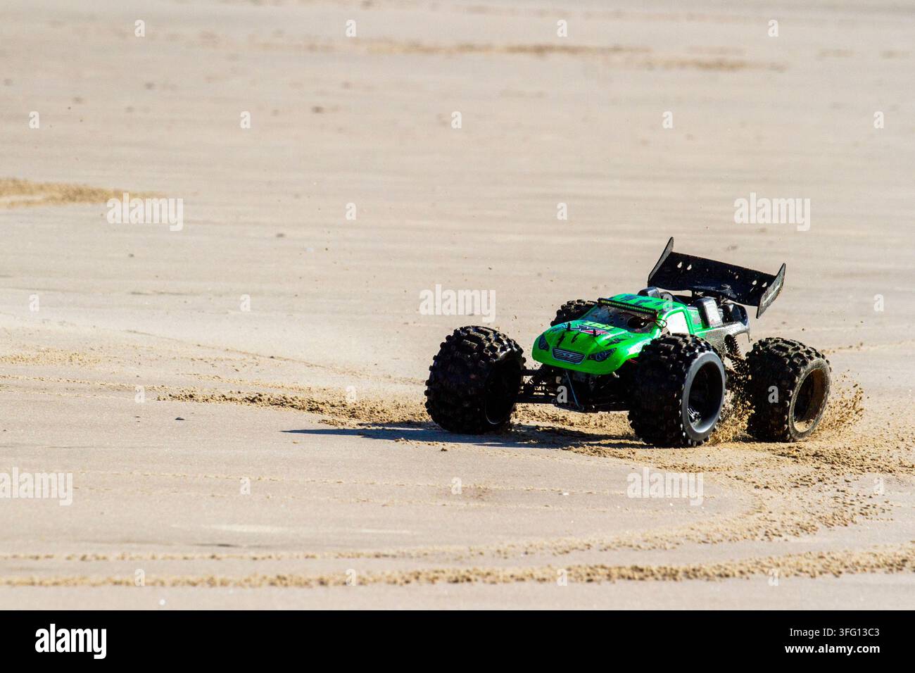 Un camion monstre télécommandé (RC) vert à grande vitesse soulève du sable en traversant une large plage de sable par une journée lumineuse et ensoleillée. Southport, Royaume-Uni. Banque D'Images