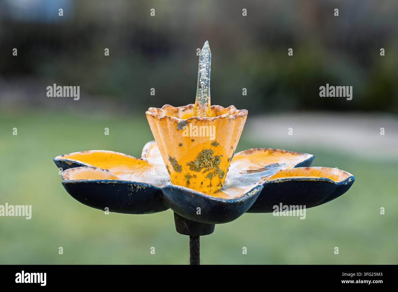 Abreuvoir pour oiseaux en fonte usée montrant une croissance de lichens et de la peinture écaillée, avec une pointe de glace transparente formée naturellement s'élevant du centre du récipient Banque D'Images