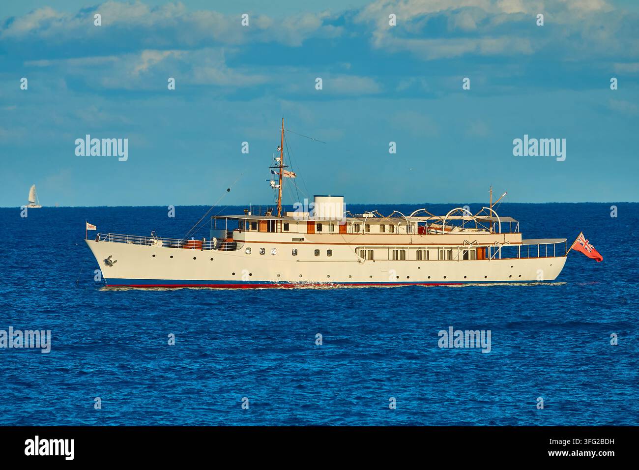 Moto-yacht classique Malahne à l'ancre sur l'océan bleu sous un ciel ensoleillé avec drapeau Red Ensign britannique Banque D'Images
