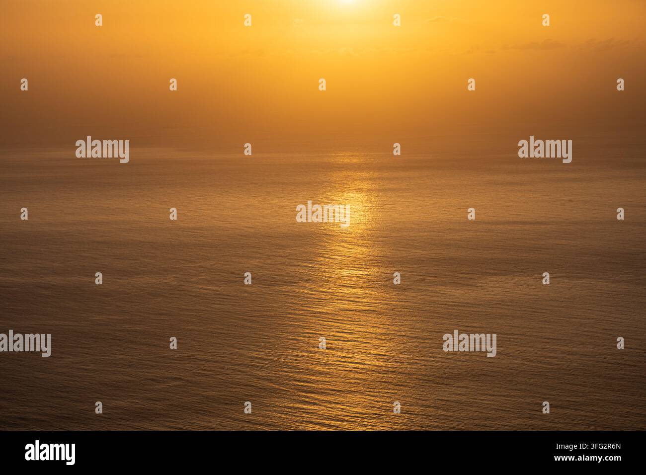 Couchant doré sur l'eau calme de l'océan avec un reflet solaire éclatant et un fond brumeux Banque D'Images