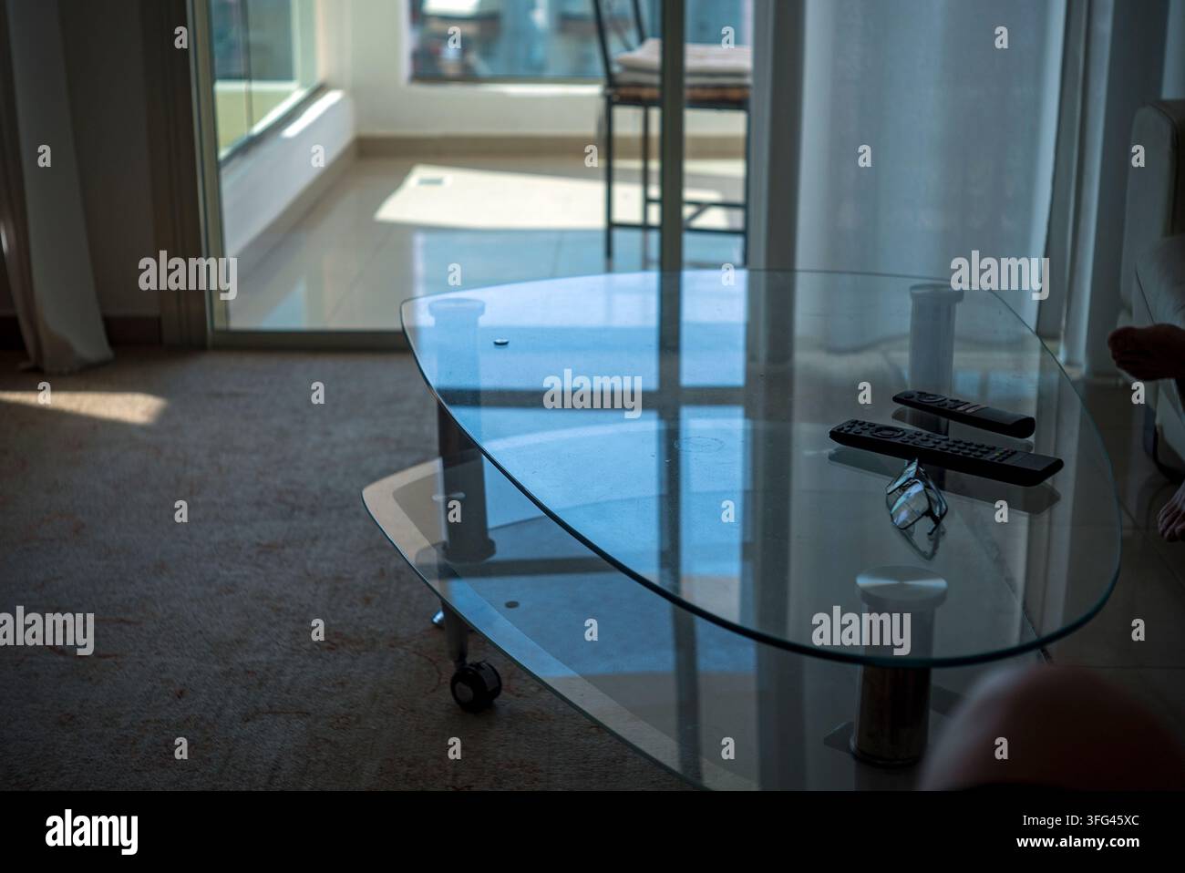 deux télécommandes sur une table en verre, des lunettes et des parties du corps de personnes, prise de vue intérieure Banque D'Images