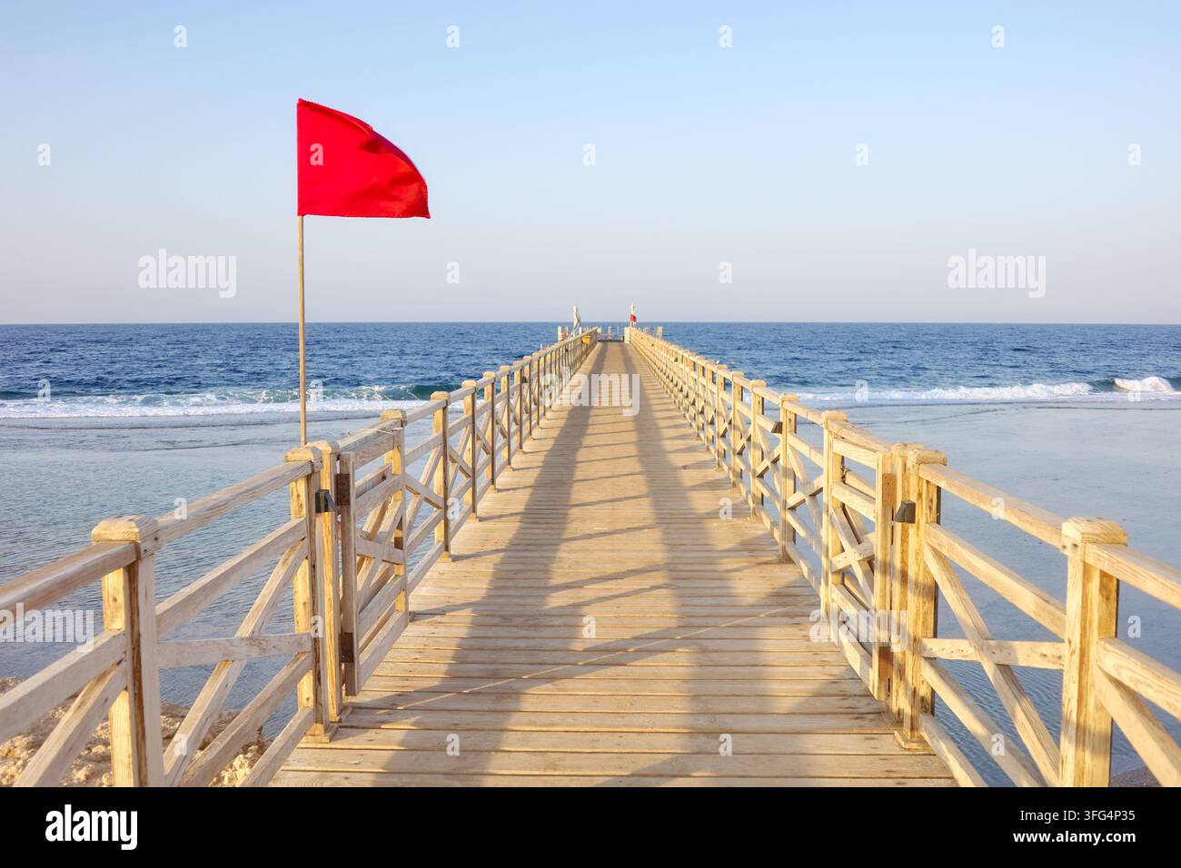 Une jetée en bois avec un drapeau d'avertissement rouge au coucher du soleil. Banque D'Images