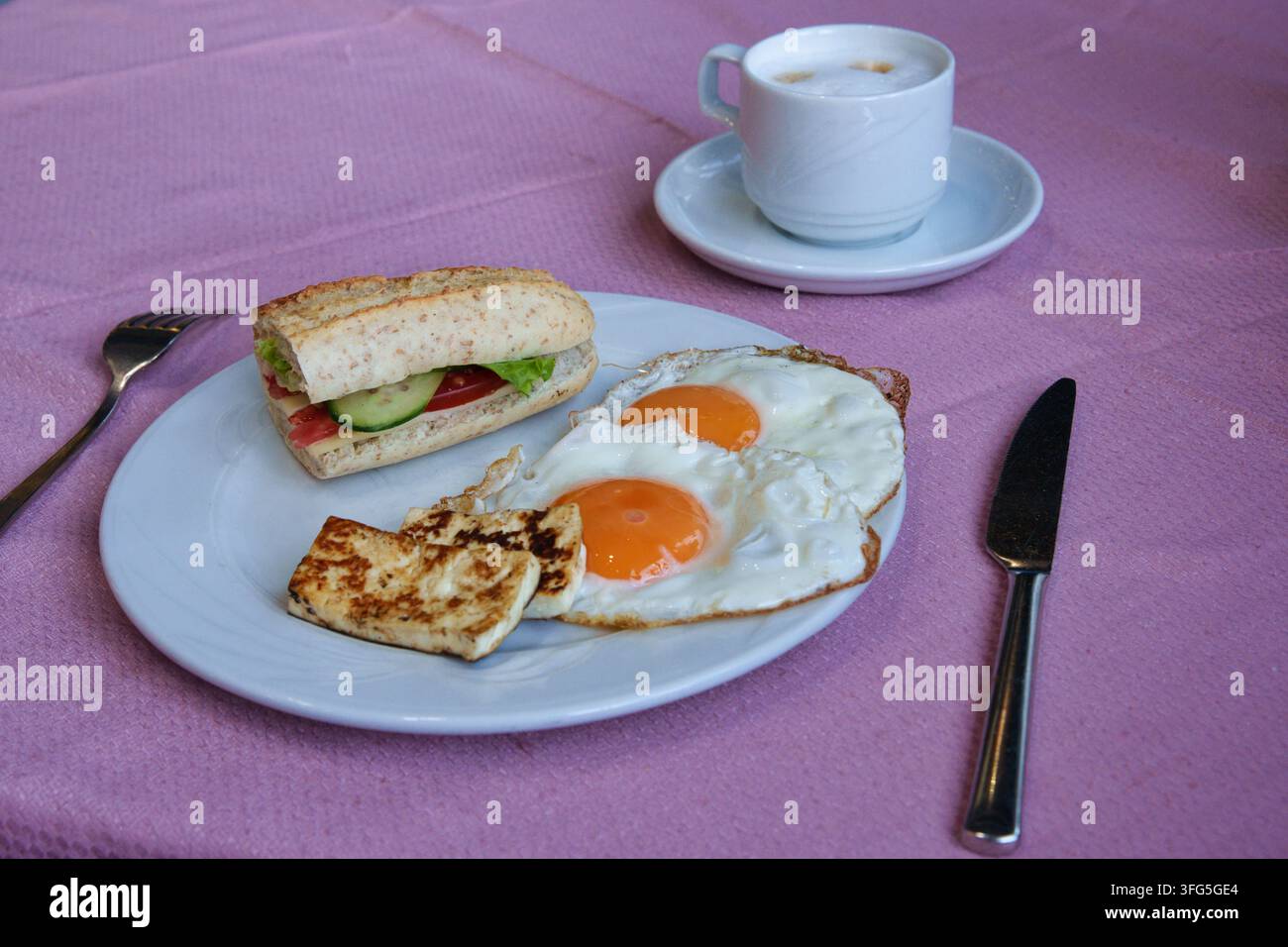 Un petit-déjeuner sain servi sur une nappe rose, comprenant une assiette blanche avec deux œufs au plat, des tranches de halloumi grillées, un Banque D'Images
