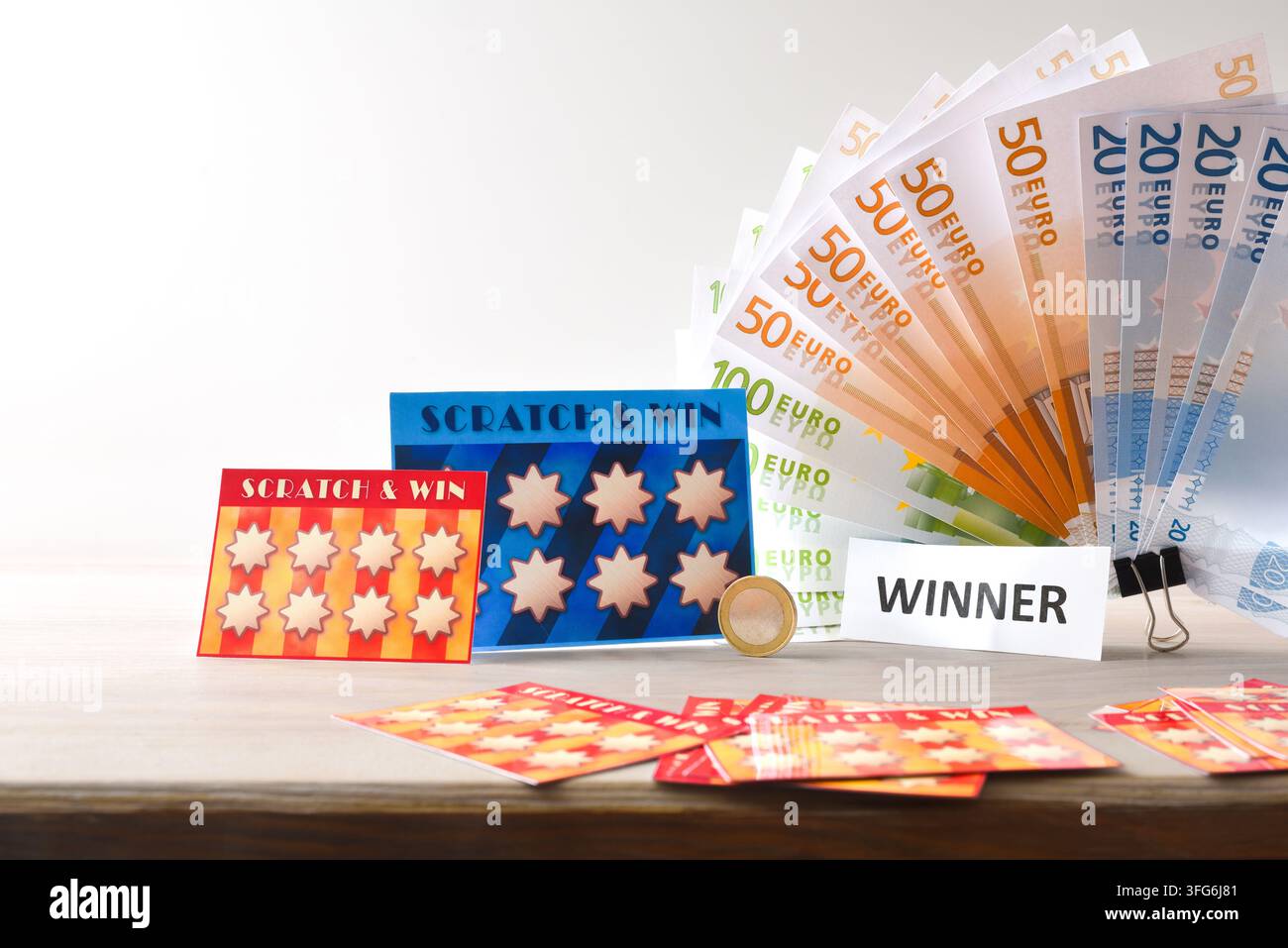 Cartes à gratter, billets en euros, un panneau de gagnant et une pièce de monnaie disposés sur une table blanche, créant une image lumineuse de succès à la loterie et de récompense financière Banque D'Images