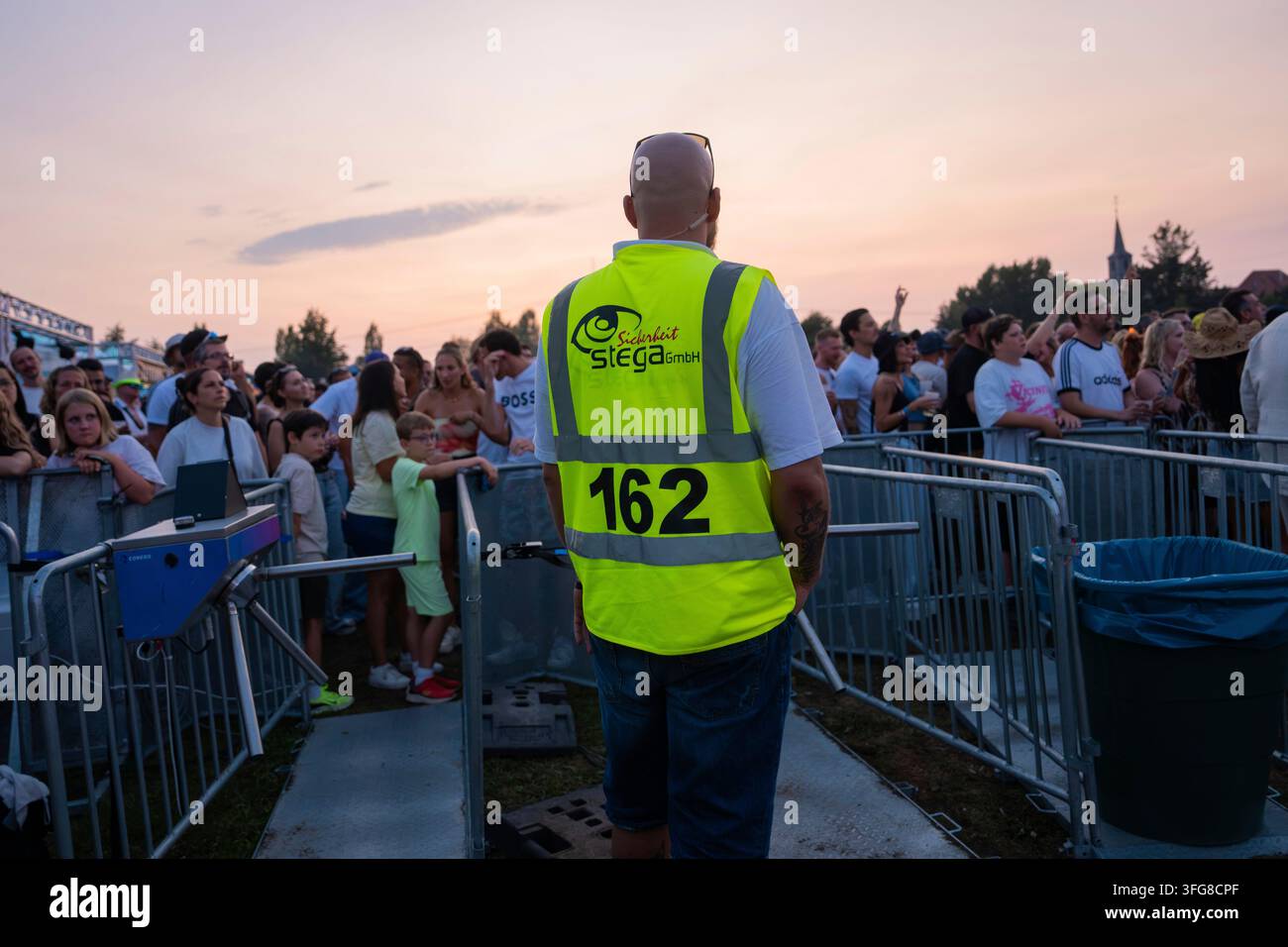 Un agent de sécurité se tient devant une foule au coucher du soleil lors d'un concert, Superjam Festival avec Stega Security, Waghaeusel, Allemagne Banque D'Images