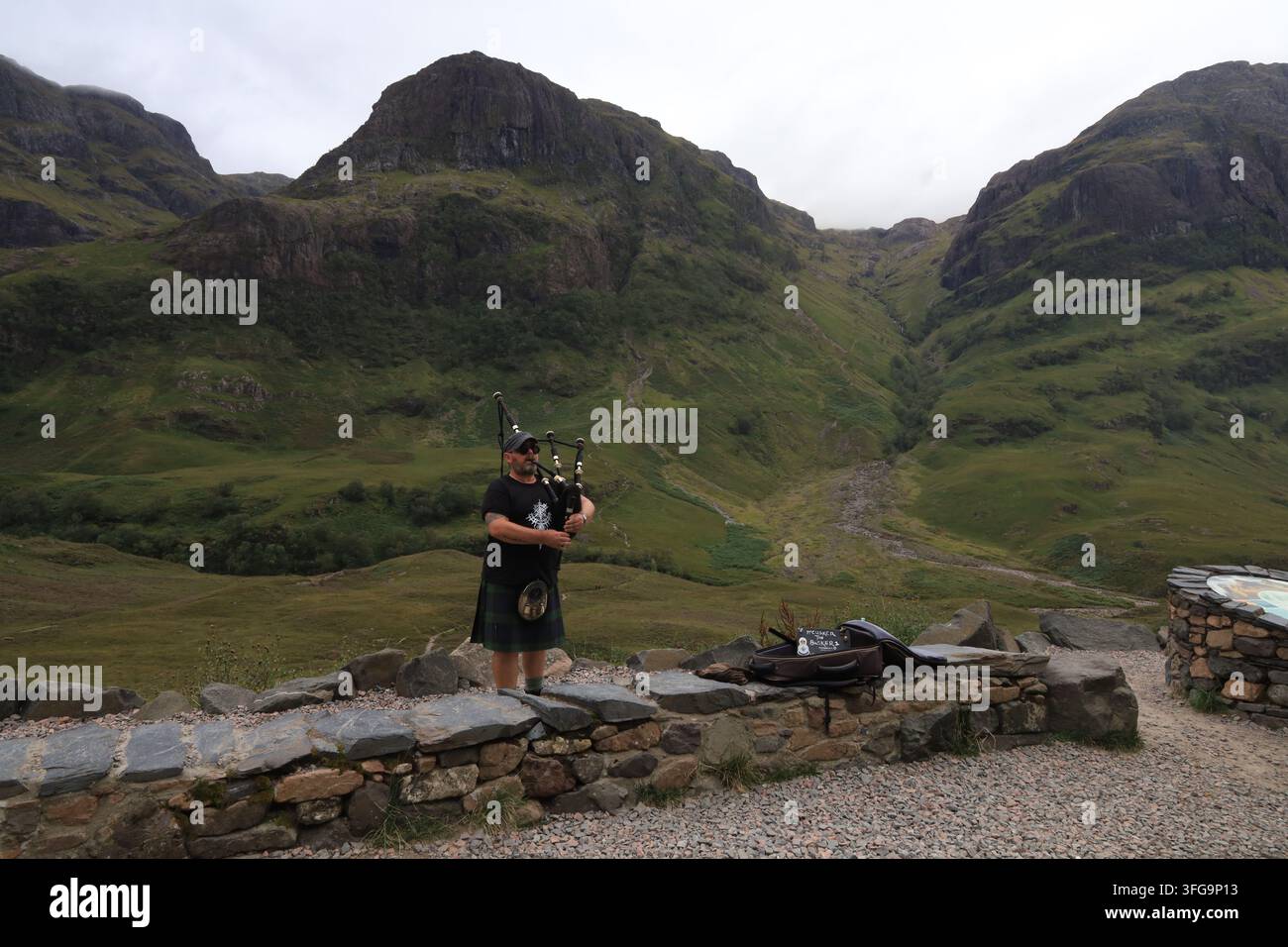 Un joueur de cornemuse écossais joue de son instrument entouré d'un paysage montagneux accidenté sous un ciel partiellement nuageux dans les Highlands écossais, août 2026. Banque D'Images