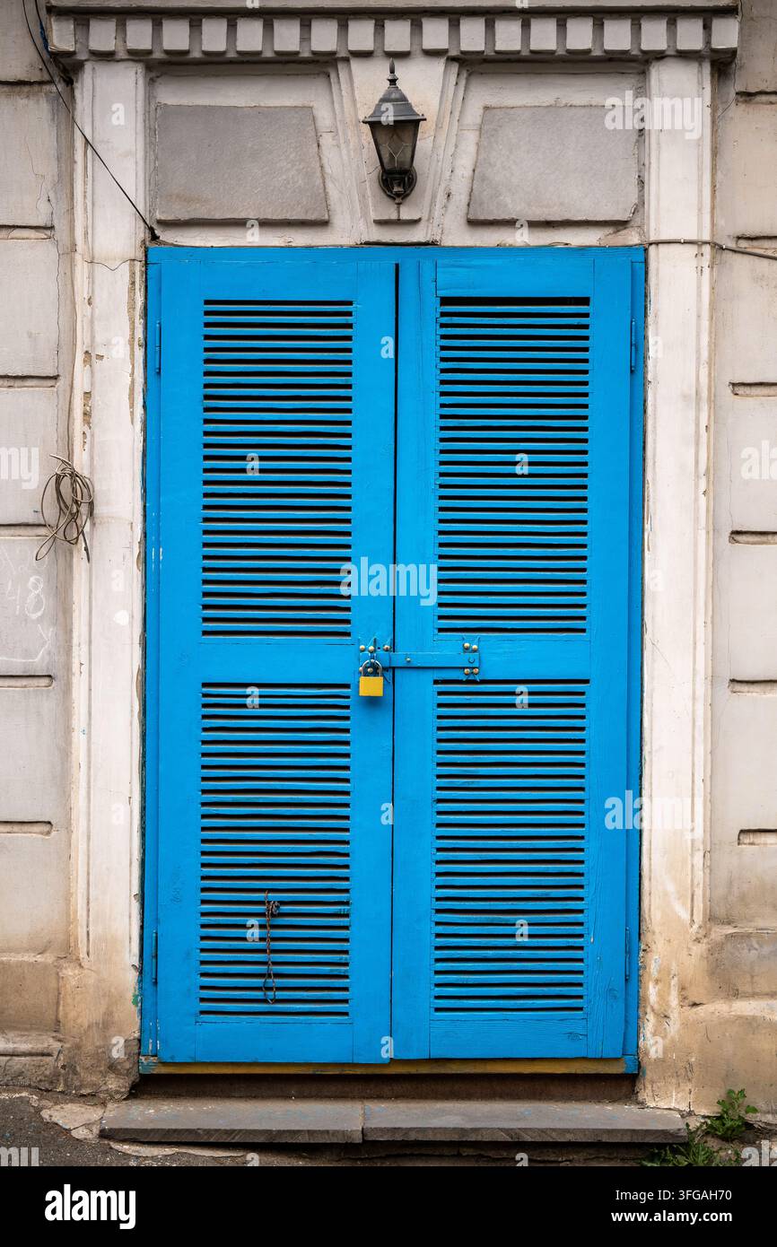 Porte en bois bleu vif avec cadenas et lanterne sur une façade de bâtiment historique érodée Banque D'Images