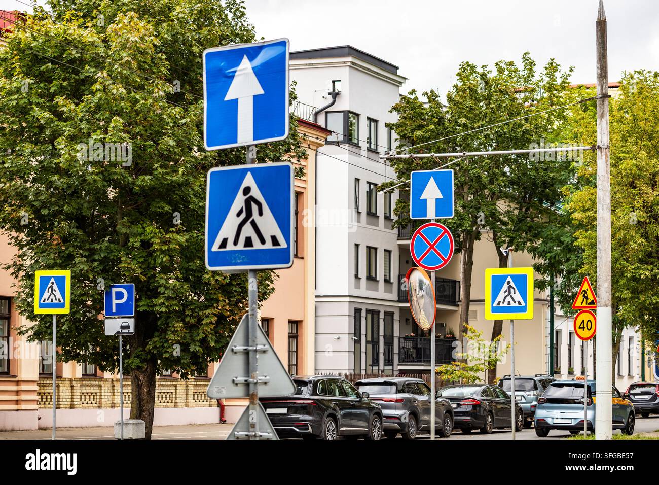 Un ensemble complexe de panneaux de signalisation routière européens comprenant un passage piéton, une rue à sens unique et une limitation de vitesse sur une route urbaine. Les voitures garées s'alignent le long Banque D'Images
