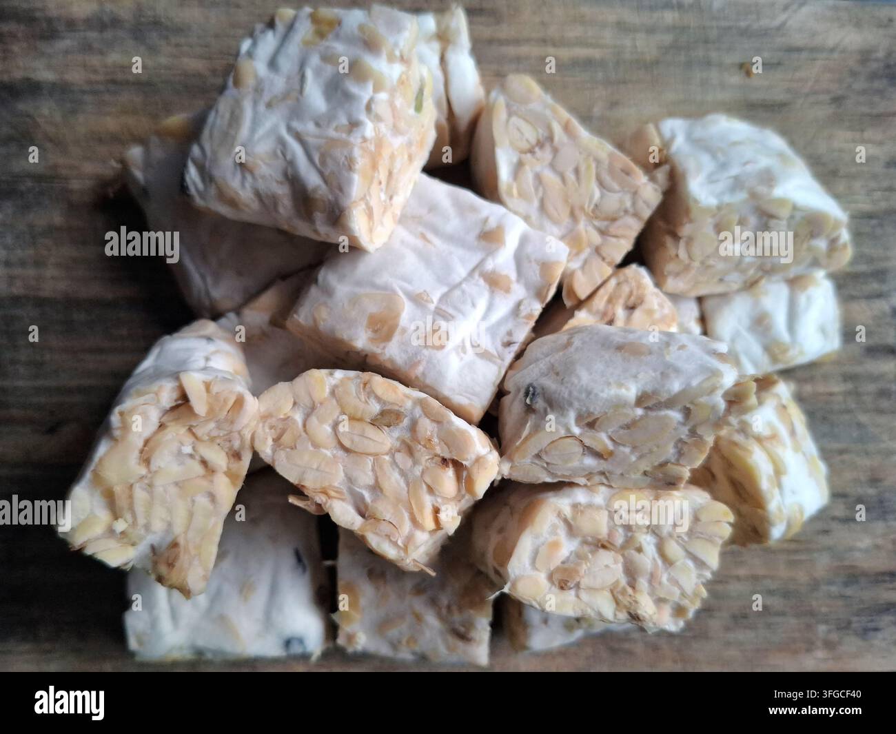 Morceaux de tempeh indonésien cru et frais empilés sur une planche à découper rustique en bois, une protéine de soja végétale populaire. Banque D'Images