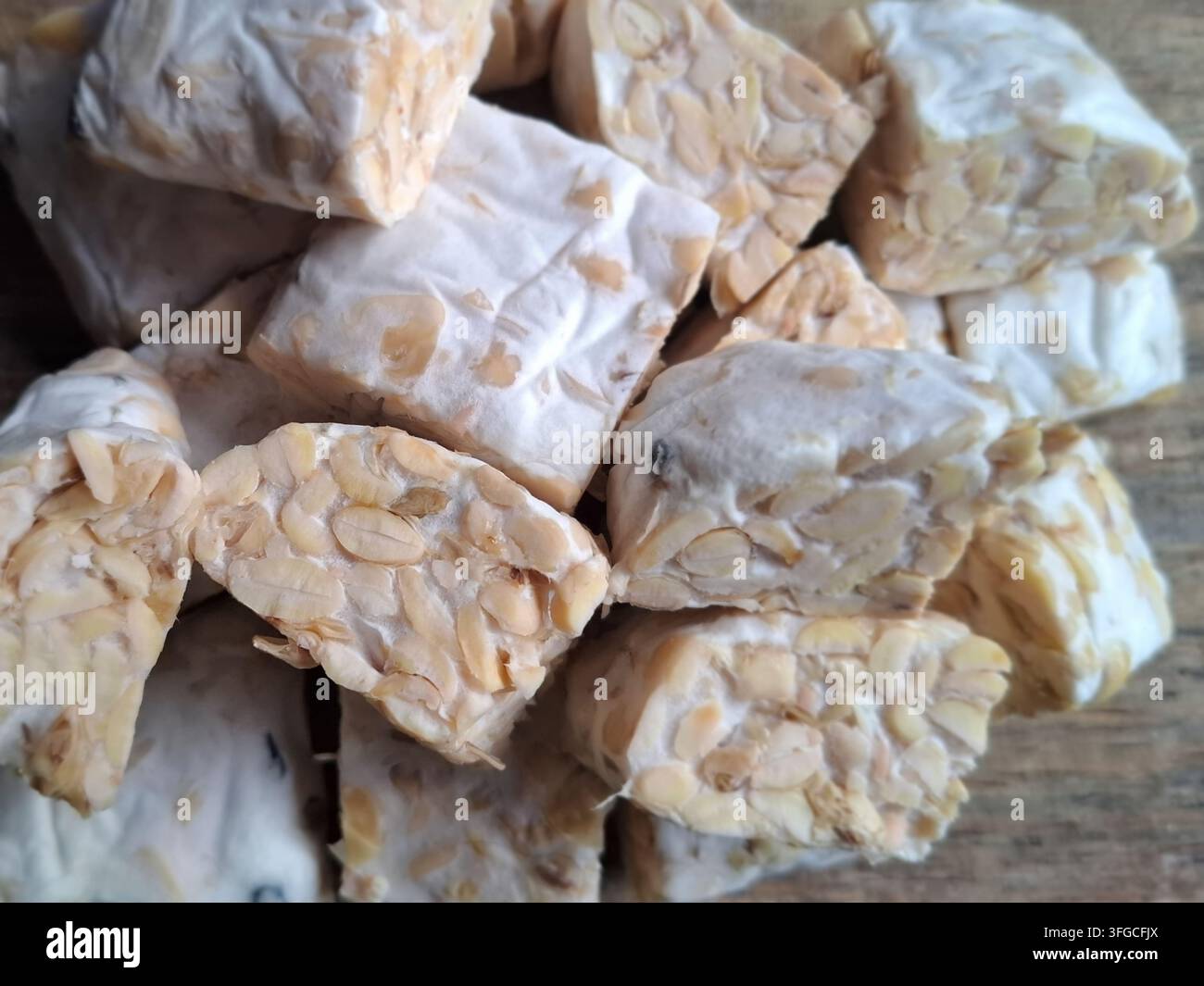 Morceaux de tempeh indonésien cru et frais empilés sur une planche à découper rustique en bois, une protéine de soja végétale populaire. Banque D'Images