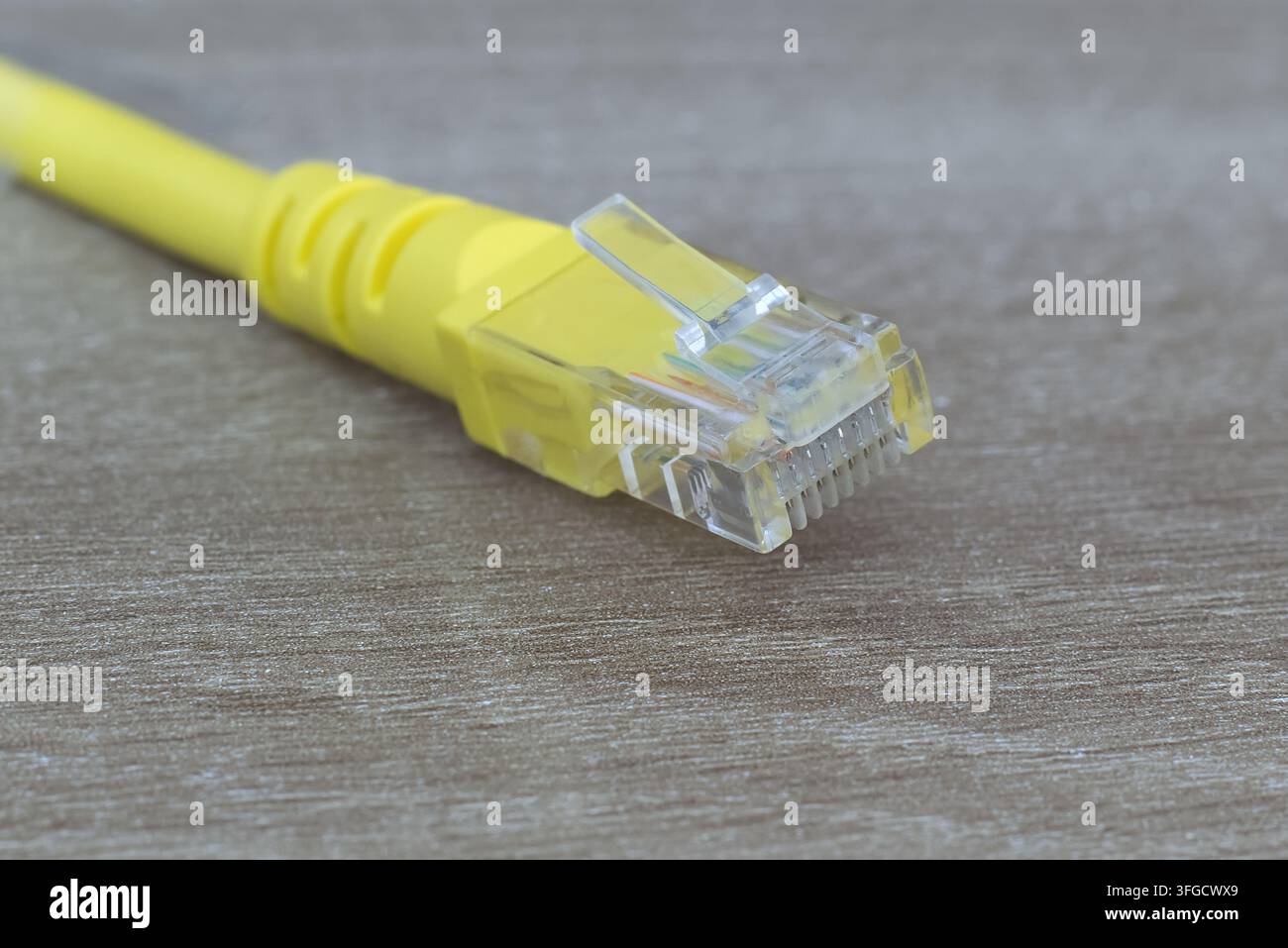 Prise de vue rapprochée détaillée d'un connecteur de câble réseau RJ45 transparent avec des broches dorées sur un fond en bois. Banque D'Images