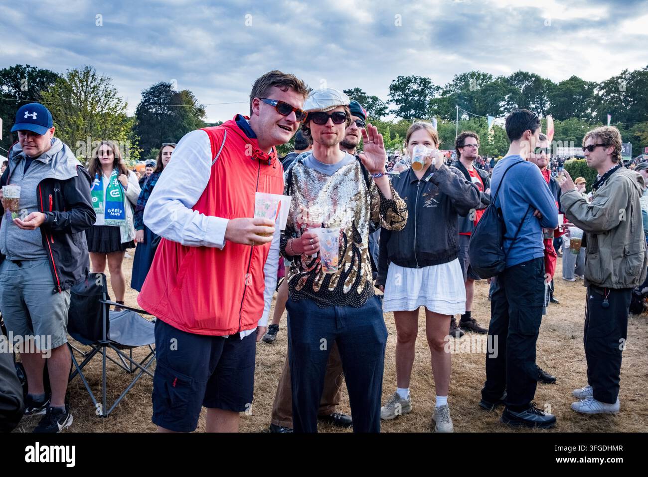 AMIS EN TENUES FUNKY À UN FESTIVAL DE MUSIQUE, REPORTAGE, GREEN MAN FESTIVAL 2026, BRECON, PAYS DE GALES, ROYAUME-UNI, 2026 : Deux hommes, l’un vêtu d’un gilet rouge et l’autre d’un haut argenté à paillettes éclatant et d’une casquette blanche, se tiennent avec des boissons dans la foule du festival, l’homme aux paillettes faisant un signe vers l’appareil photo. Photo : Rob Watkins. INFO : Le Green Man Festival se tient dans les Brecon Beacons en août. Il célèbre la musique alternative, les arts, la littérature, la science et une culture adaptée aux familles dans un magnifique cadre montagneux. L’événement de 2026 a eu lieu pendant des orages à la fin d’une longue vague de chaleur et d’une sécheresse. Banque D'Images