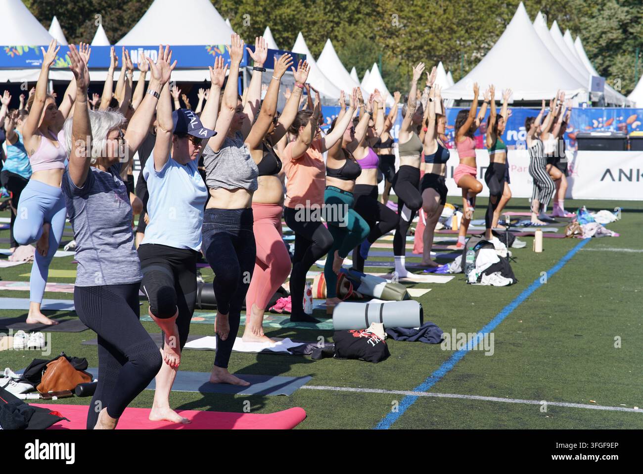 Grand groupe de femmes participant à une séance d'échauffement de yoga avant l'événement de course féminine La Parisienne sur un terrain extérieur à Paris, France. Banque D'Images