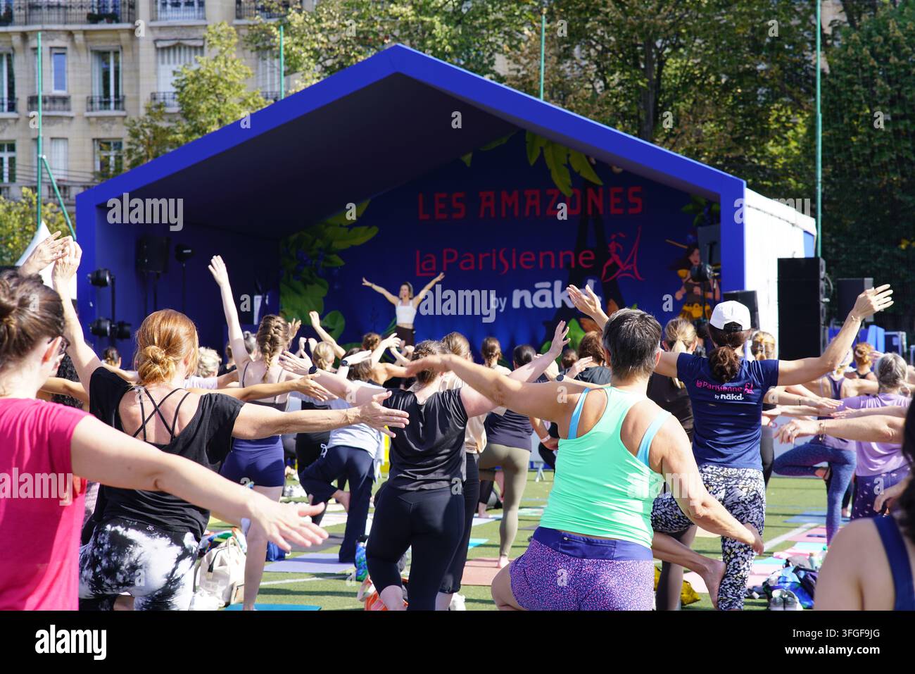 Grand groupe de femmes participant à une séance d'échauffement de yoga avant l'événement de course féminine La Parisienne sur un terrain extérieur à Paris, France. Banque D'Images
