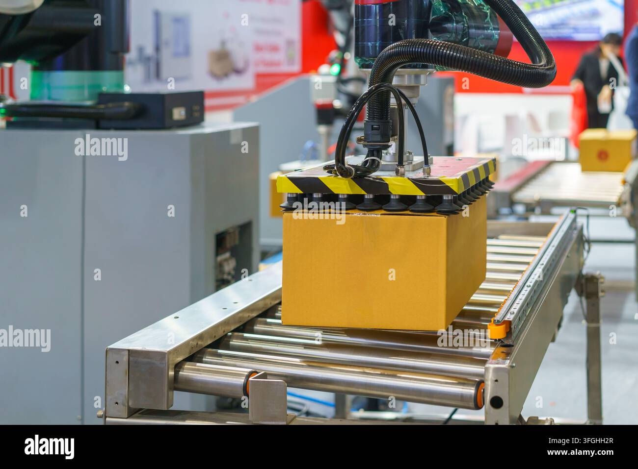 Brazo robotisé automatisé utilisant des ventouses à vide pour soulever et déplacer une boîte en carton marron le long d'un convoyeur à rouleaux dans une logistique ou une manufacture moderne Banque D'Images