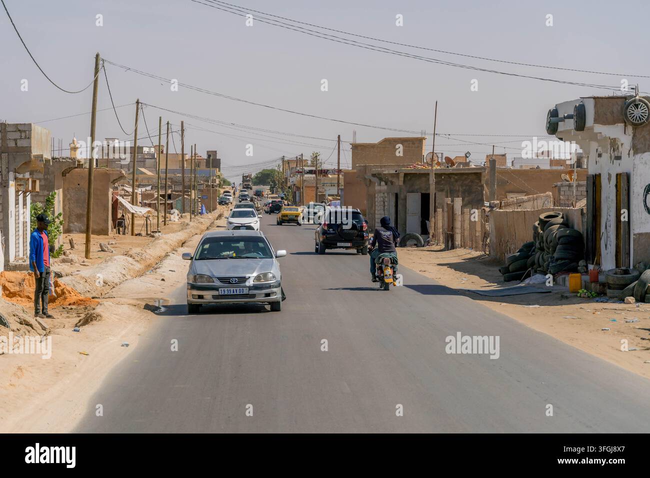 La circulation se déplace le long d'une route en asphalte poussiéreuse à l'extérieur de Nouakchott, en Mauritanie, où le sable dériveant, les déchets et les conditions désertiques posent des défis au transport rural. Banque D'Images