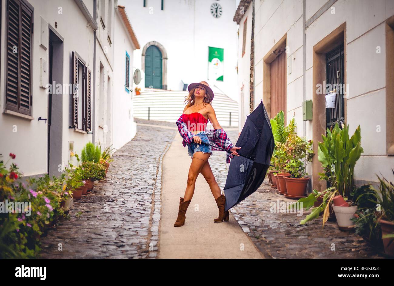 Une femme élégante tenant un parapluie ouvert tout en marchant dans une ruelle pavée traditionnelle bordée de maisons blanchies à la chaux à Cachopo Banque D'Images