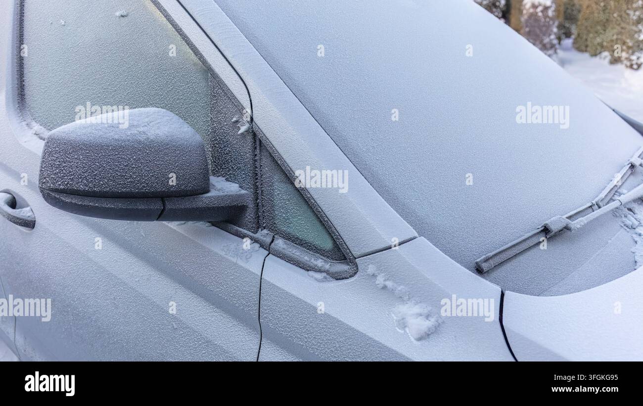 L'exposition nocturne du véhicule laisse une voiture de tourisme argentée recouverte d'un givre dense sur son pare-brise, son rétroviseur latéral et sa carrosserie, illustrant un matin froid Banque D'Images