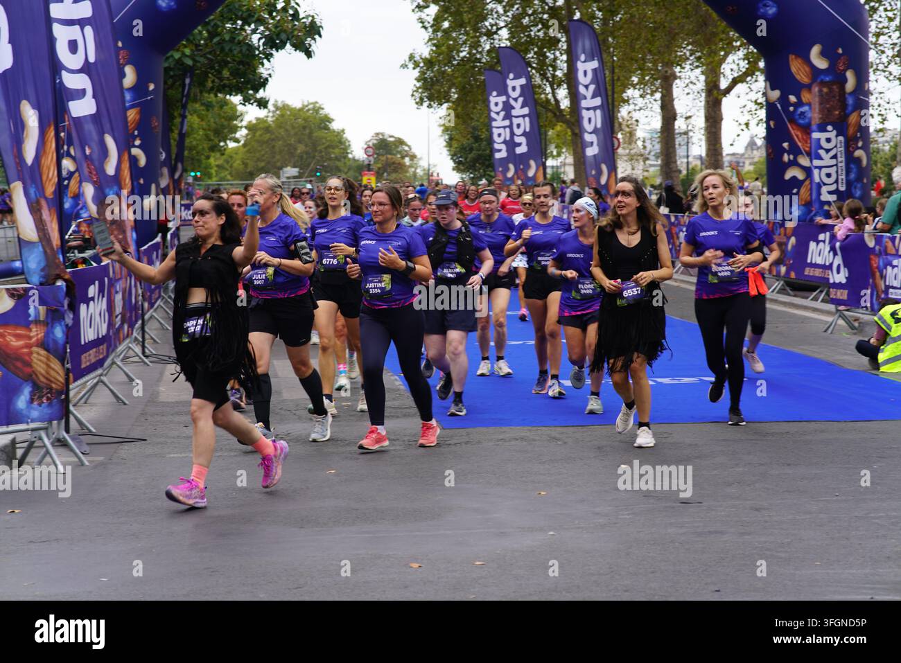 Coureuses en tenues festives assorties célébrant à l'arrivée de l'événement de course féminine La Parisienne sur une rue de Paris en France. Banque D'Images
