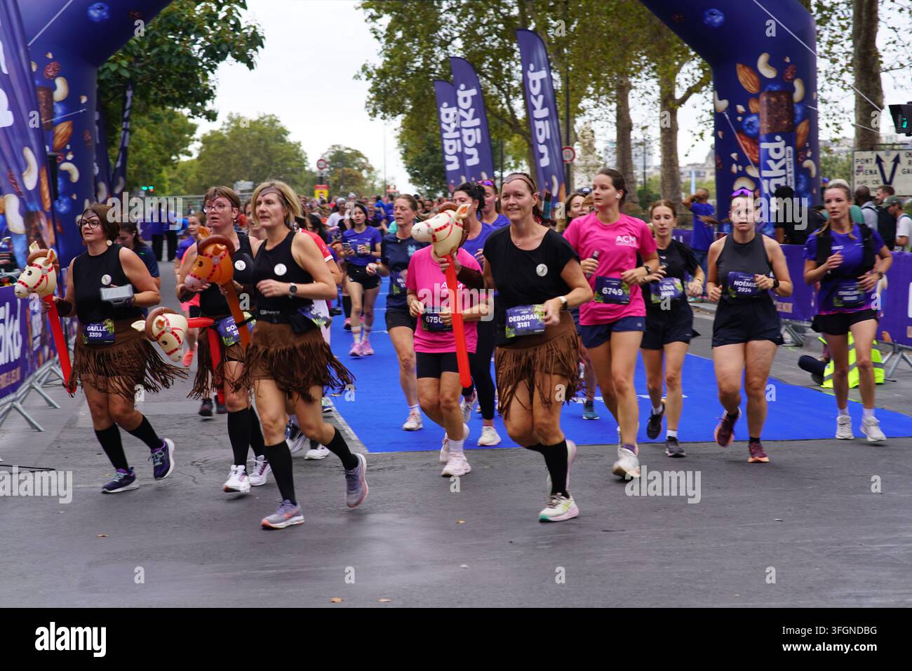 Coureuses en tenues festives assorties célébrant à l'arrivée de l'événement de course féminine La Parisienne sur une rue de Paris en France. Banque D'Images
