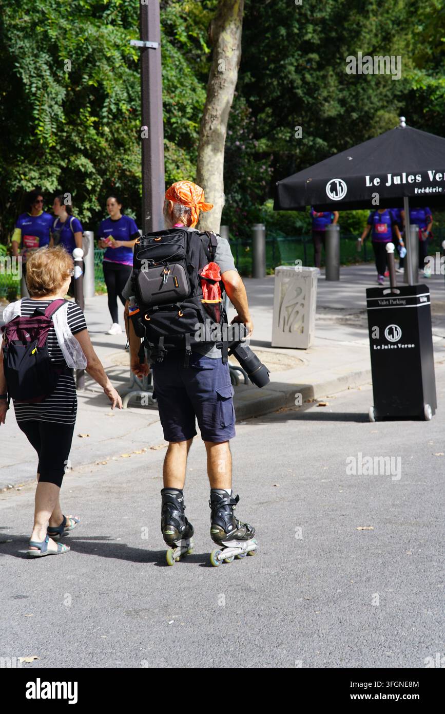 Homme en patins à roulettes portant du matériel photographique à côté des participantes lors de l'événement de course féminine La Parisienne à Paris, France. Banque D'Images