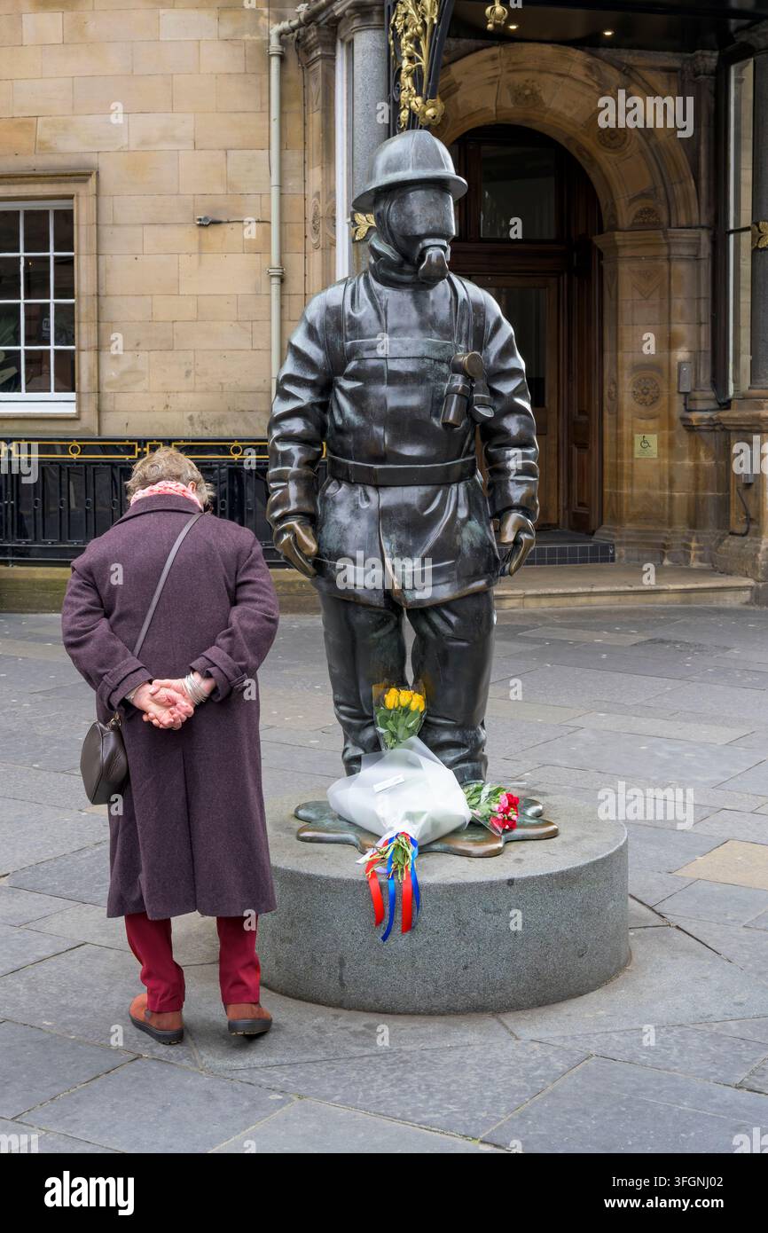 Une femme regardant des fleurs déposées sur la sculpture Citizen Firefighter à l'occasion du 25e anniversaire des attentats du 11 septembre, Gordon Street, Glasgow, Écosse, Royaume-Uni Banque D'Images