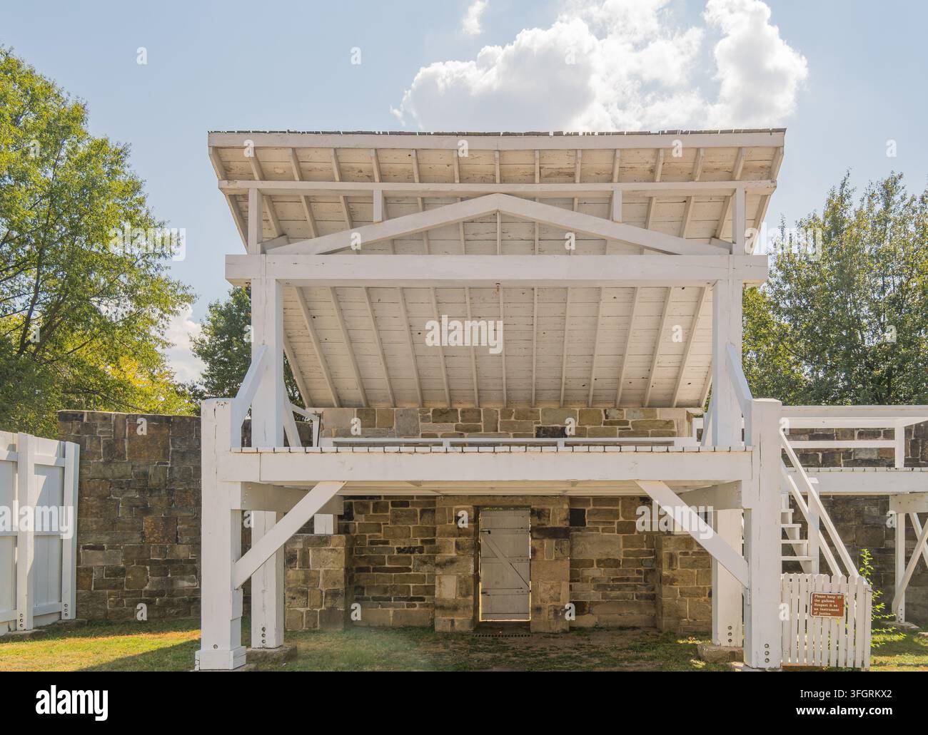 Un abri en bois blanc protège des ruines en pierre sous un ciel bleu nuageux. Banque D'Images