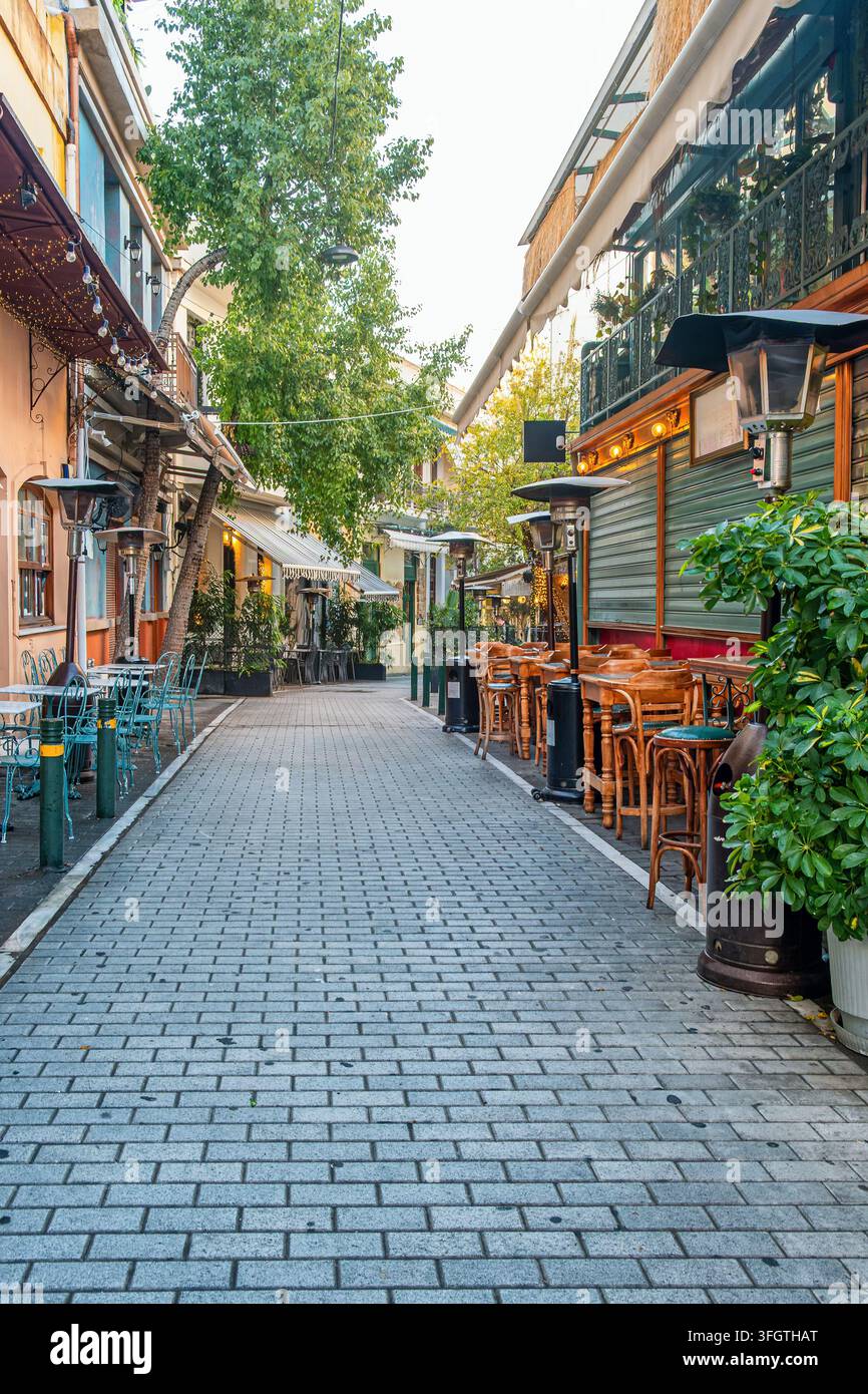 Rue piétonne avec cafés en terrasse, terrasses de restaurants, tables en bois, arbres et bâtiments traditionnels à Athènes, Grèce. Tourisme urbain Banque D'Images