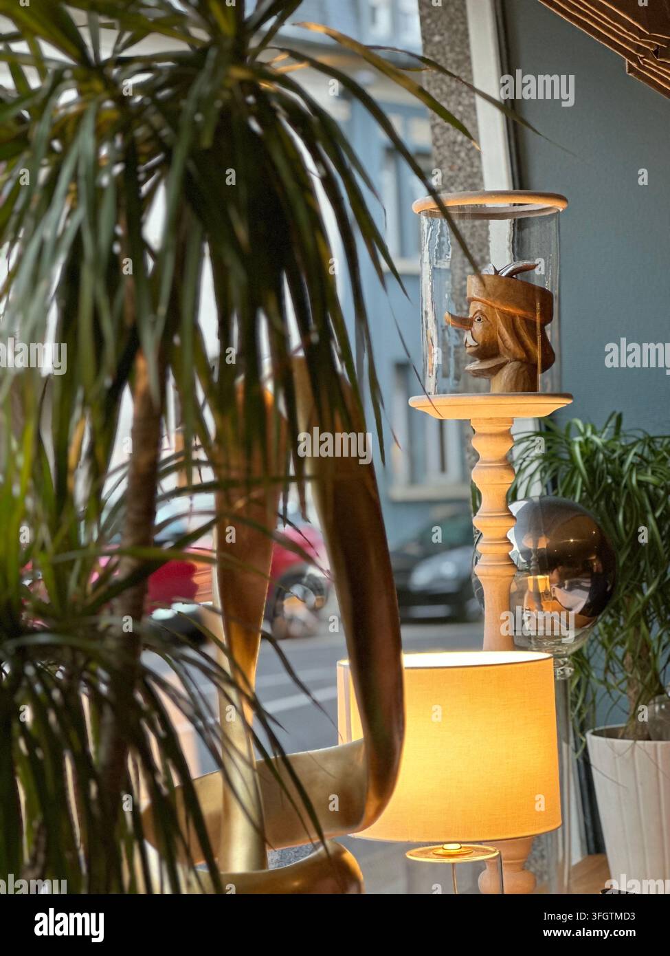 Vue intérieure d'une fenêtre mettant en vedette une tête de poupée en bois sous verre et des plantes vertes. Configuration intérieure confortable de fenêtre avec une figurine de poupée en bois sculpté enfermée - Image de stock capturée avec un smartphone