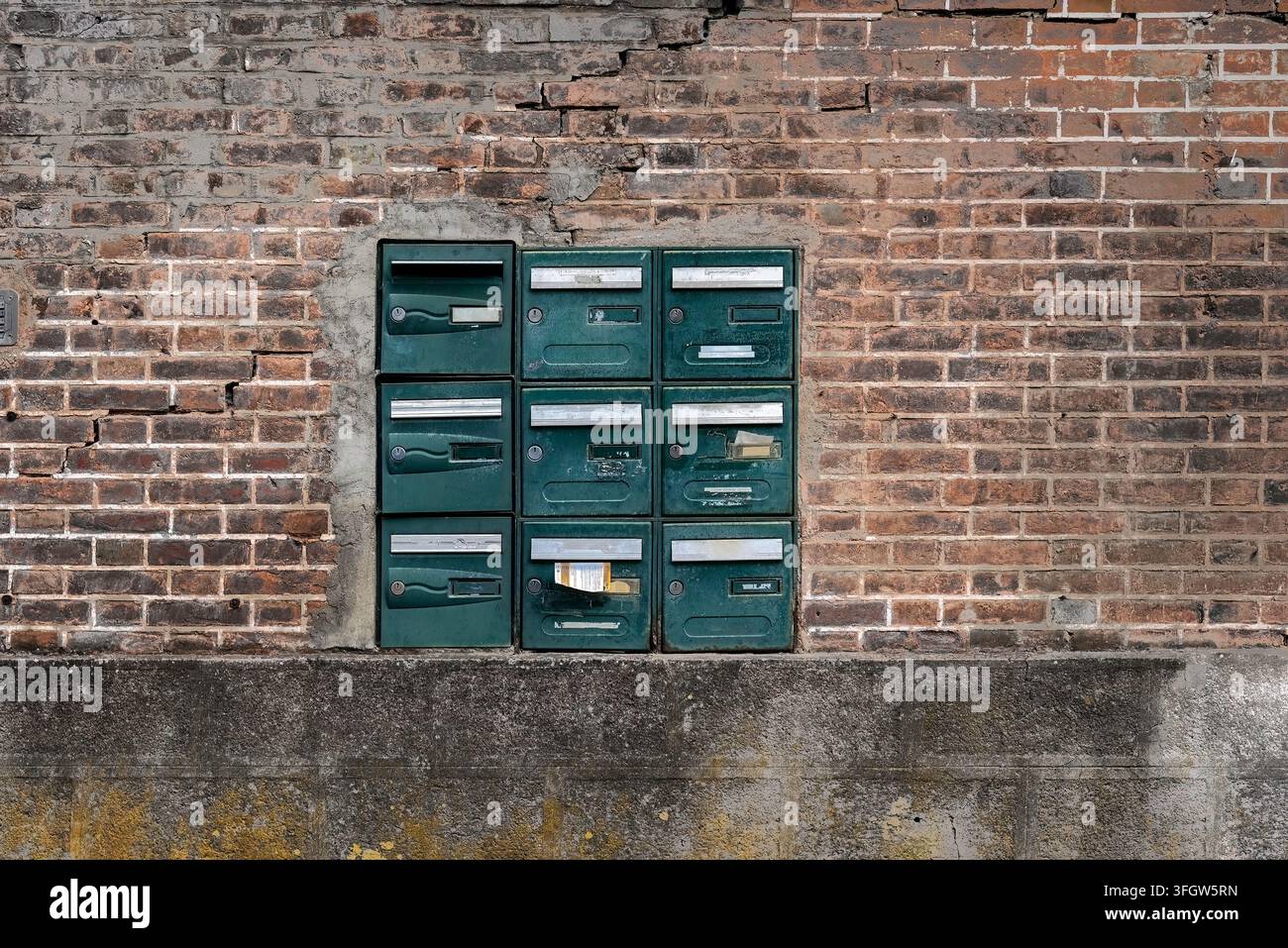 Un bloc de neuf boîtes aux lettres en métal vert à l'ancienne avec des fentes pour les noms encastrées dans un mur de briques rouges patiné. Banque D'Images