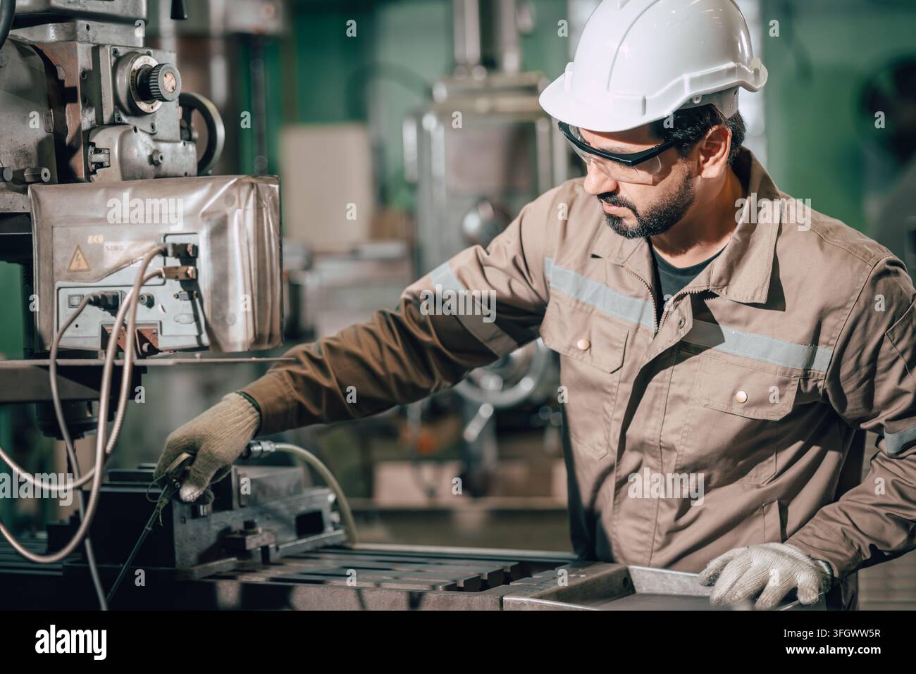 Homme indien utilisant un souffleur d'air pour le nettoyage de maintenance des déchets métalliques sur une table de fraisage dans l'industrie lourde du métal après le travail. Banque D'Images