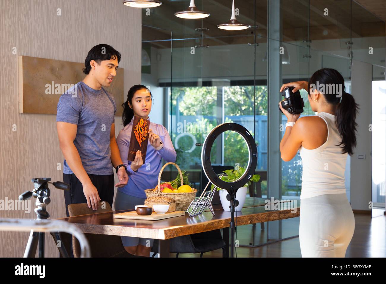 Équipe diversifiée en tenue de gym préparant un shooting de dîner à domicile, montrant des aliments emballés avec un DSLR, lumière annulaire Banque D'Images