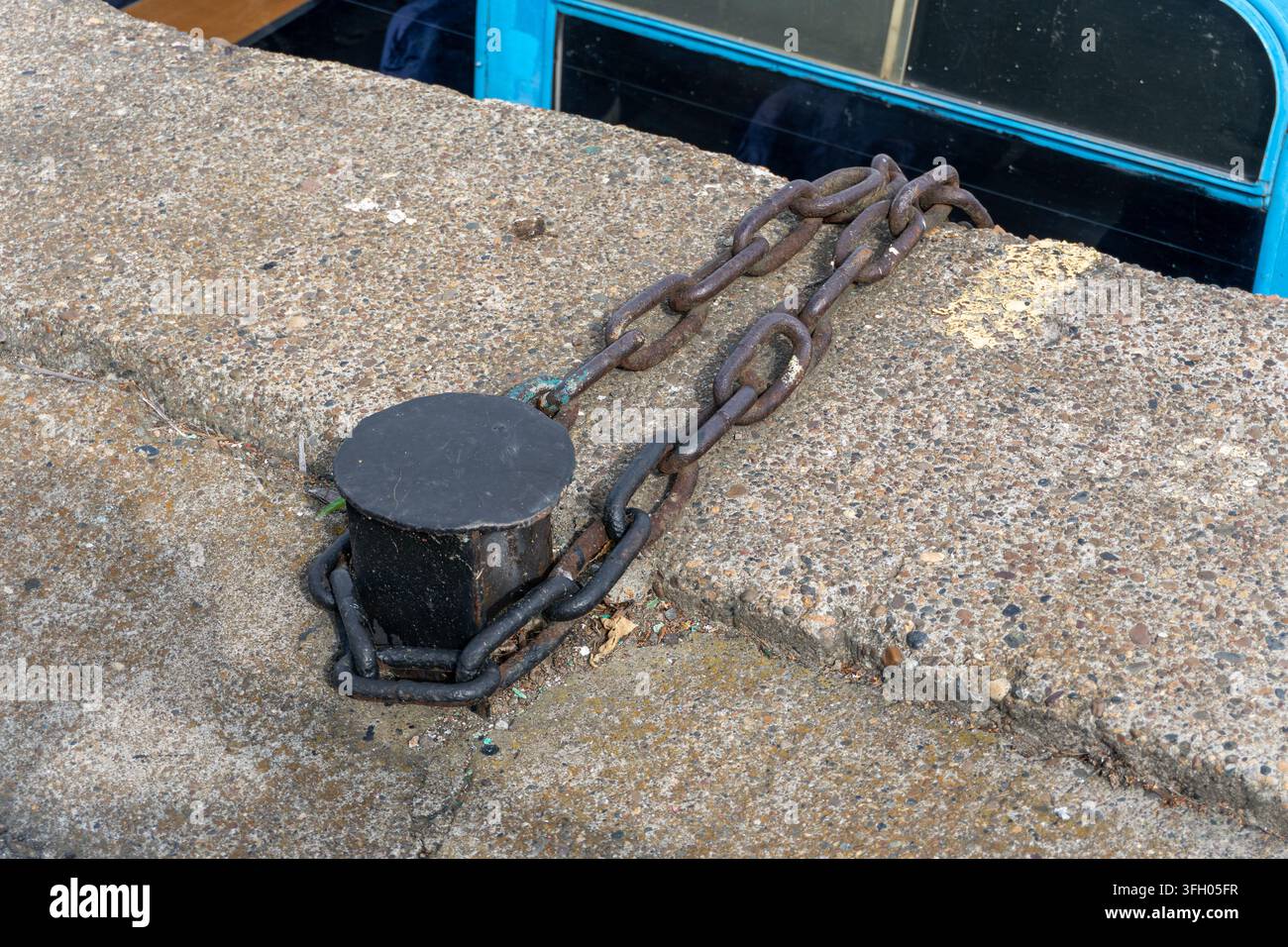 Petite anneau d'amarrage en métal avec chaîne sur un quai en béton Banque D'Images