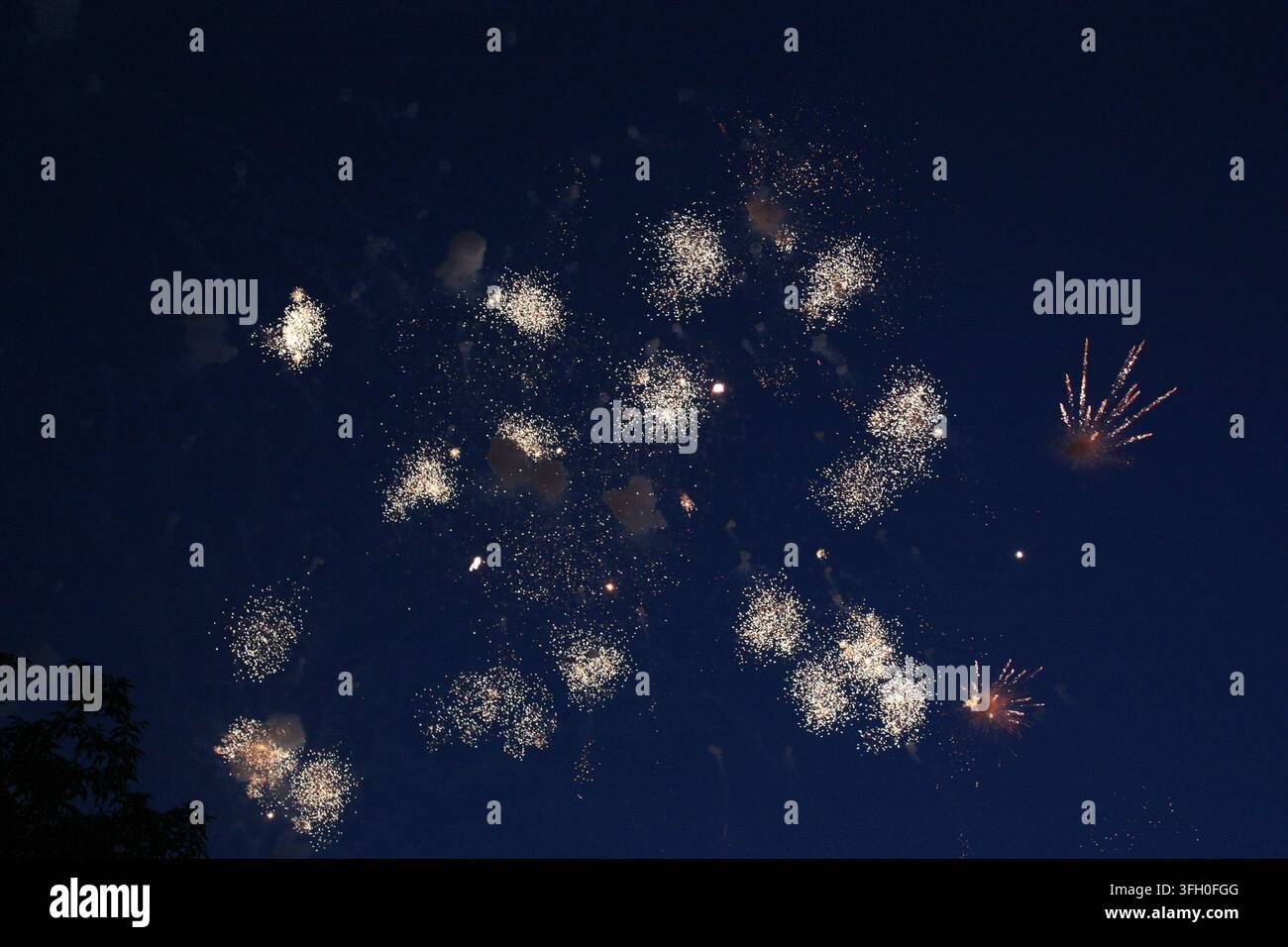 Un magnifique spectacle de feux d'artifice comprenant de nombreuses petites explosions dispersant des nuages de paillettes blanches éclatantes dans le ciel nocturne. Banque D'Images