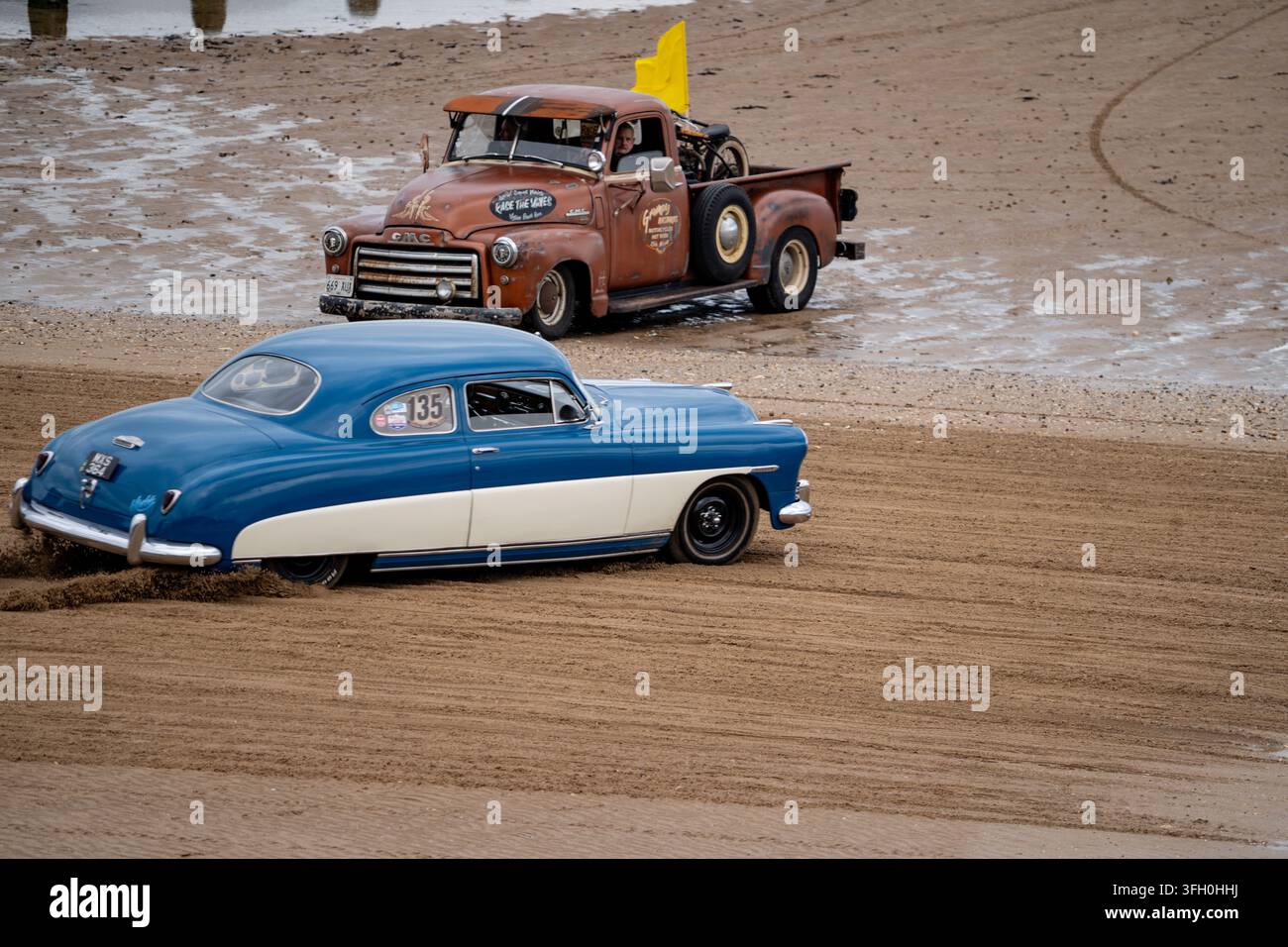 Hot rod bleu personnalisé et camion rat rod GMC rouillé en course sur la plage sud de Bridlington lors de Race the Waves 2026 Banque D'Images