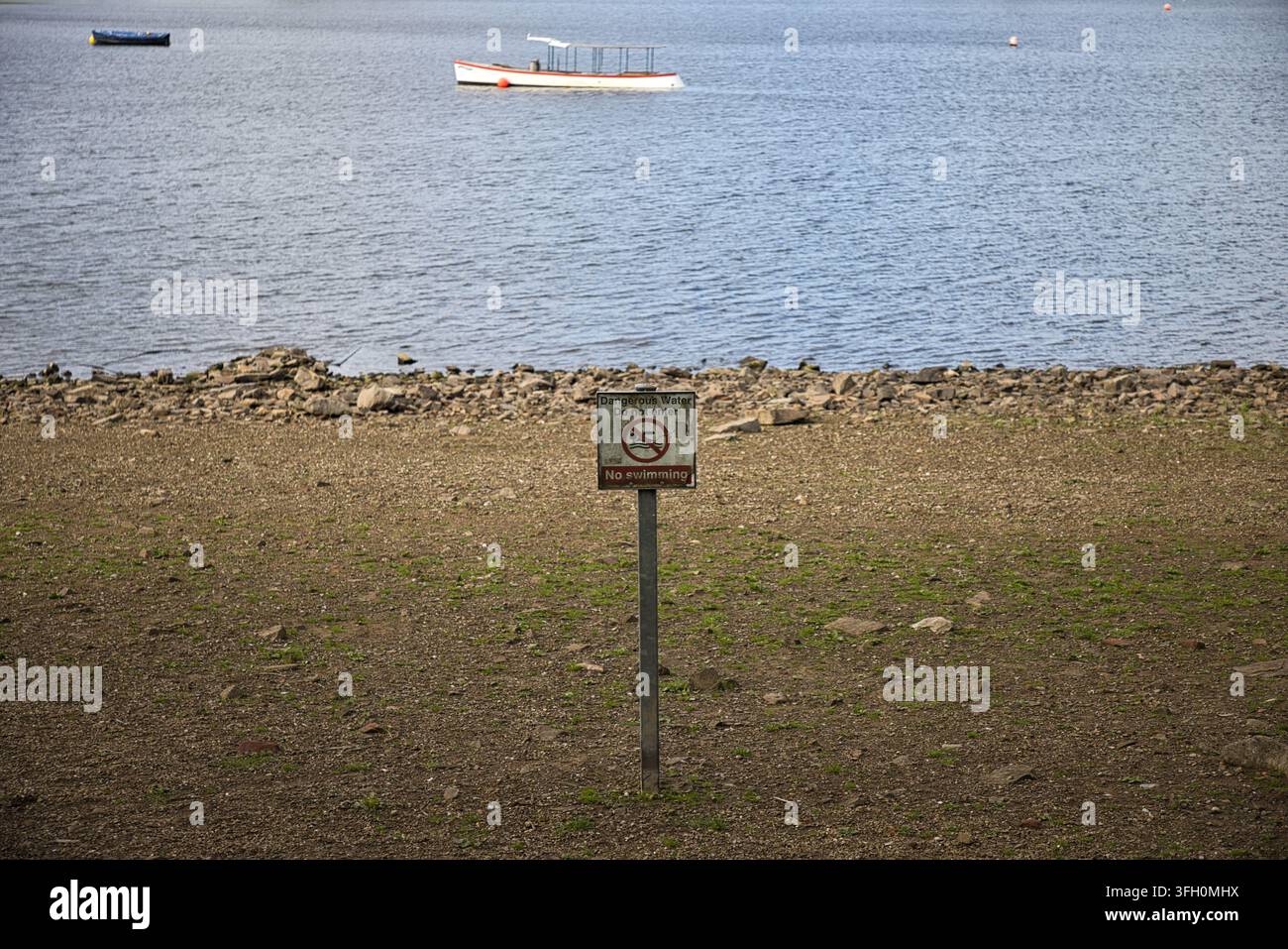 Panneau d'avertissement "Eau dangereuse, Interdiction d'entrer, Pas de baignade" sur le rivage de galets du lac Hollingworth avec des bateaux sur l'eau, Rochdale, Royaume-Uni. Banque D'Images