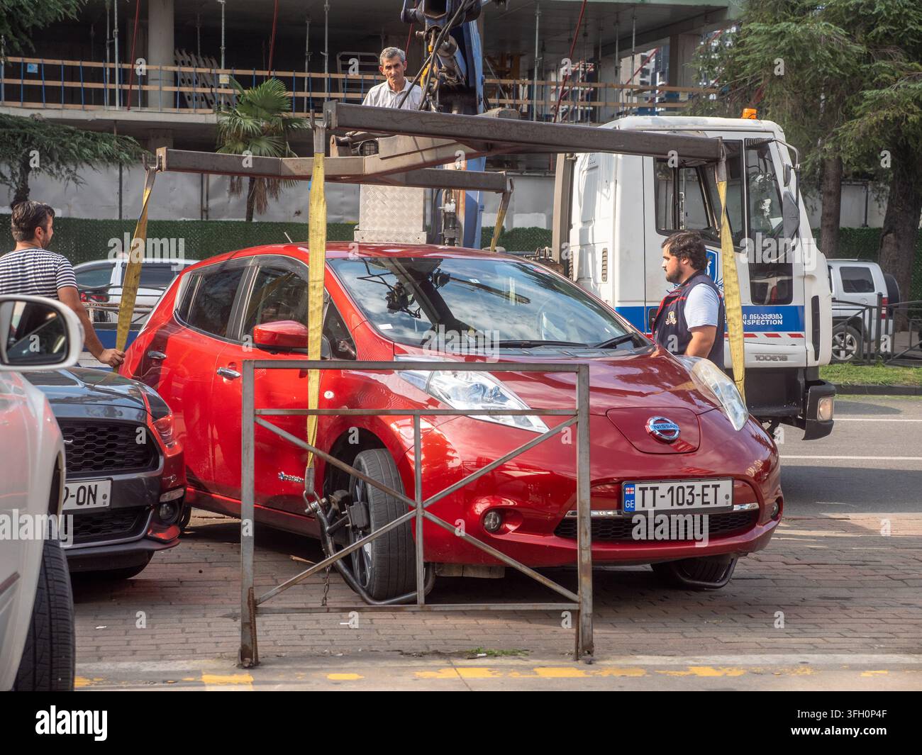 Batumi, Géorgie – 14 septembre 2026 : des agents de contrôle des parkings municipaux remorquent une Nissan Leaf électrique rouge d’une rue de la ville de Batumi. Banque D'Images