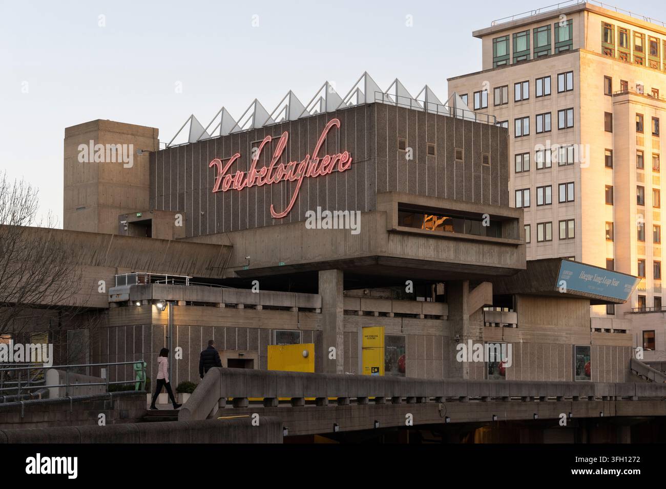 Des gens passent devant la Hayward Gallery du Southbank Centre à Londres en hiver, présentant l'installation artistique au néon lumineuse "You Belong Here". Banque D'Images