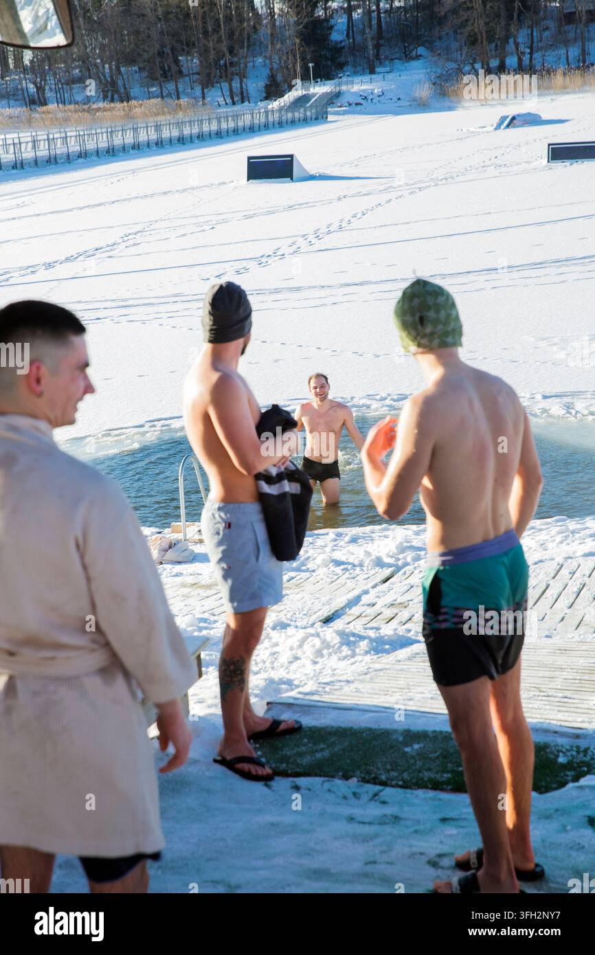 Les hommes appréciant la thérapie de plongée froide dans le trou de glace de lac gelé, bien-être social, biohacking d'hiver, récupération active, jour d'hiver ensoleillé, aventure Banque D'Images
