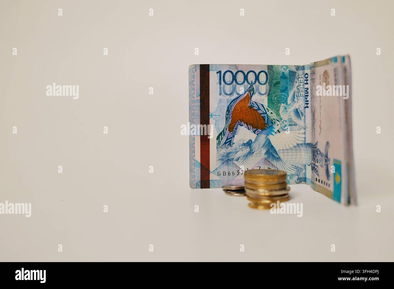 Billetes de tenge kazakh pliés avec des pièces de monnaie affichés sur un fond neutre minimal, créant un concept commercial épuré pour la devise, banque Banque D'Images