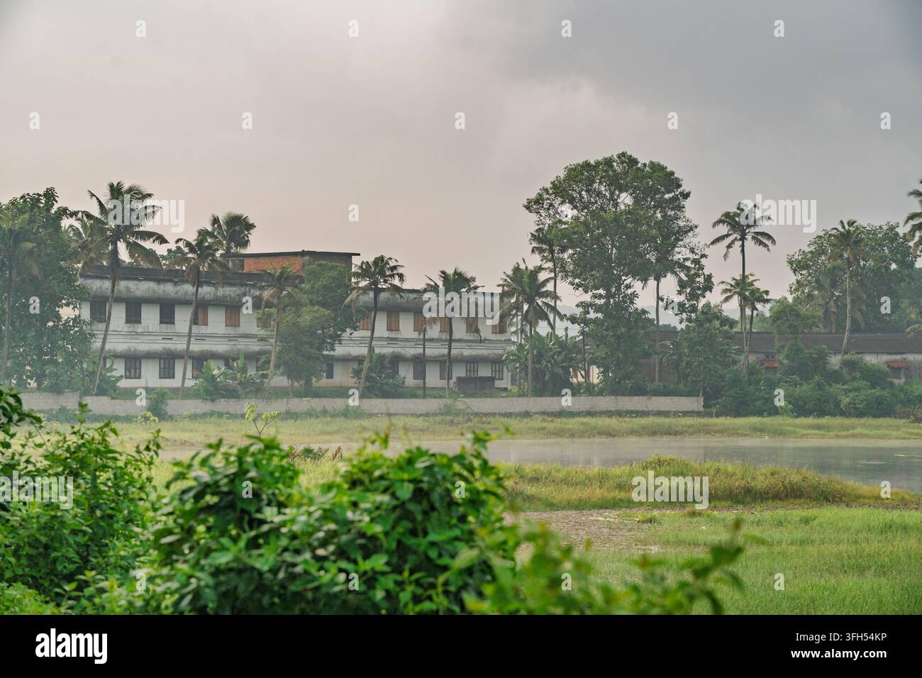 Kerala, Inde – 18 août 2026 : Vue lointaine du bâtiment de l’école secondaire supérieure Mount Carmel à travers un plan d’eau à Mathilakam Banque D'Images
