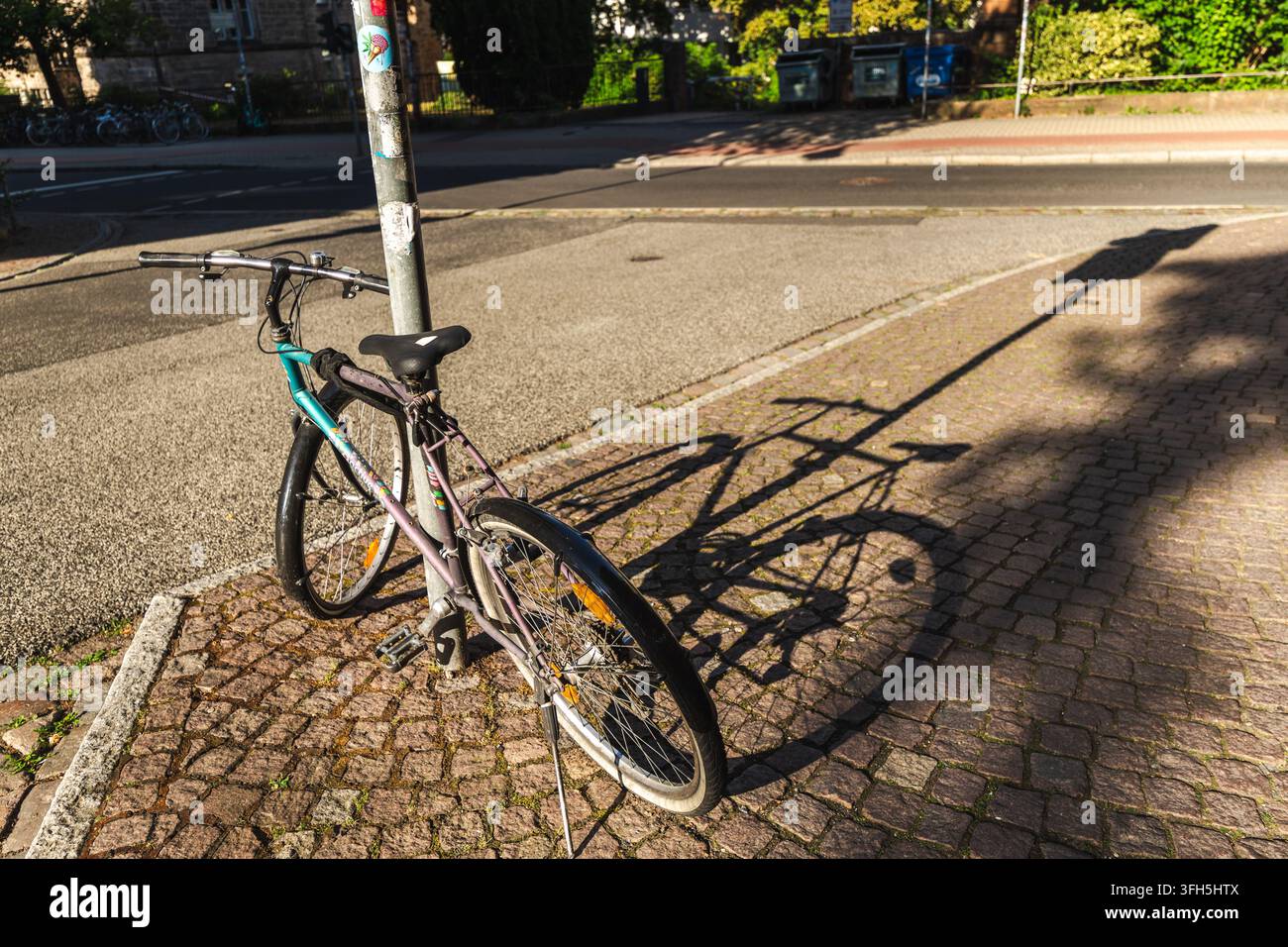 Vélo garé projetant une longue ombre à côté d'une rue ensoleillée à Marburg Banque D'Images