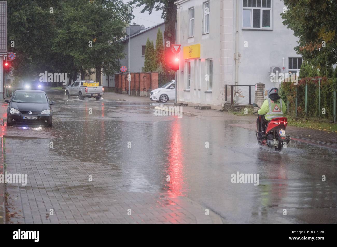 VALMIERA, LETTONIE - 1er SEPTEMBRE 2026 : Apprenti motard roule sous une forte pluie sur une rue mouillée de la ville pendant une formation de moto Banque D'Images